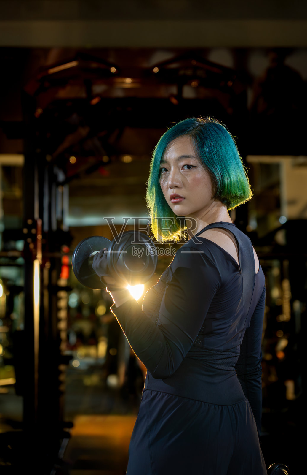 时尚发型亚洲女子单手举哑铃,在现代健身房进行有力的锻炼照片摄影图片
