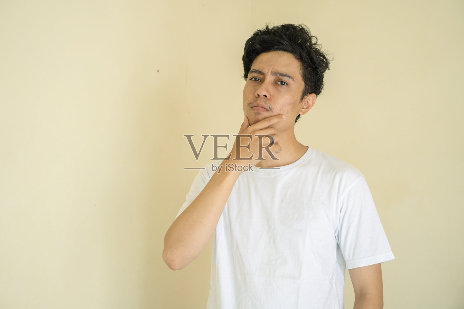 年轻卷曲的男子穿着白色t恤思考手势和表情。照片摄影图片