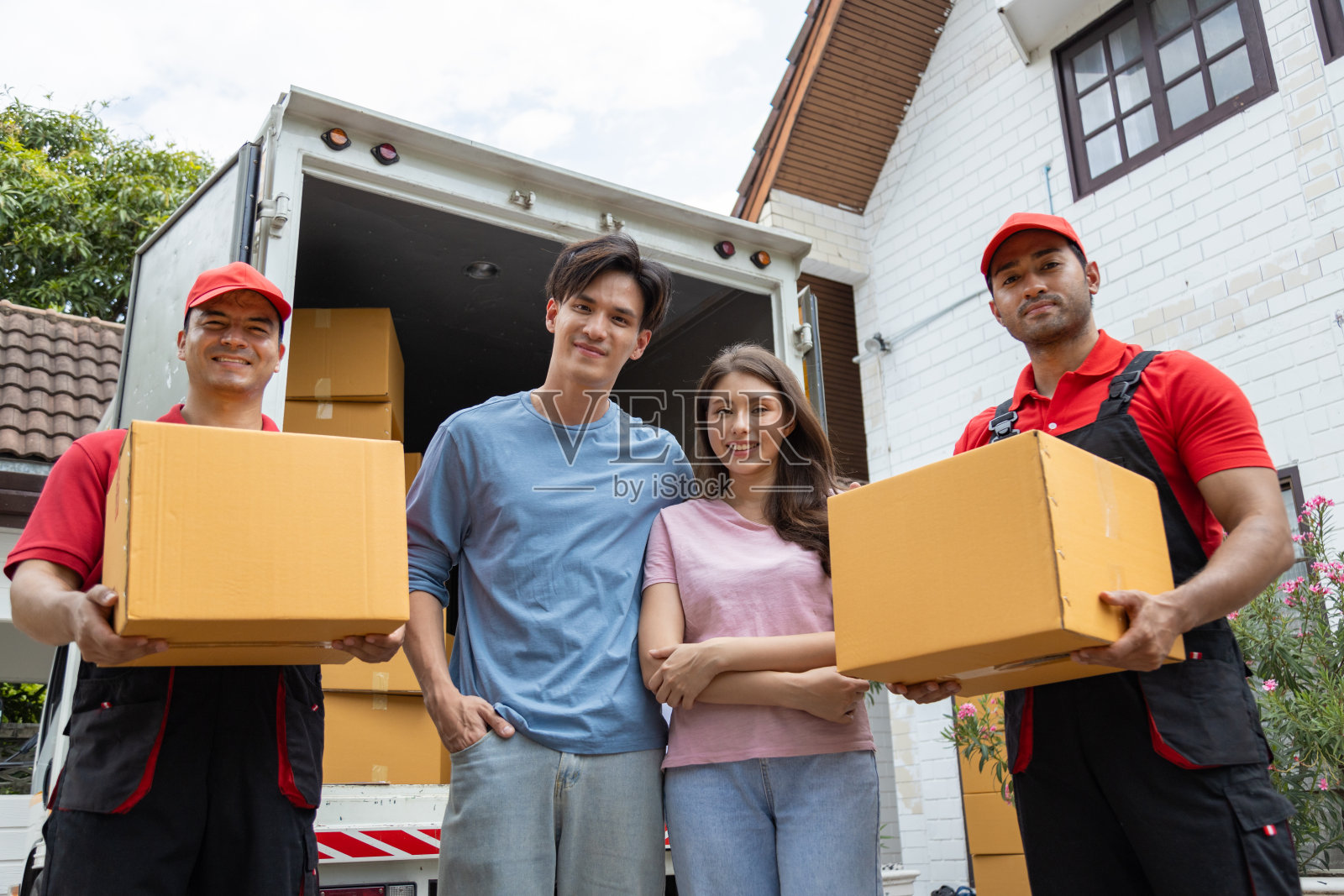 一对年轻夫妇和两个从皮卡车上卸下箱子和家具的搬运工核对照片摄影图片