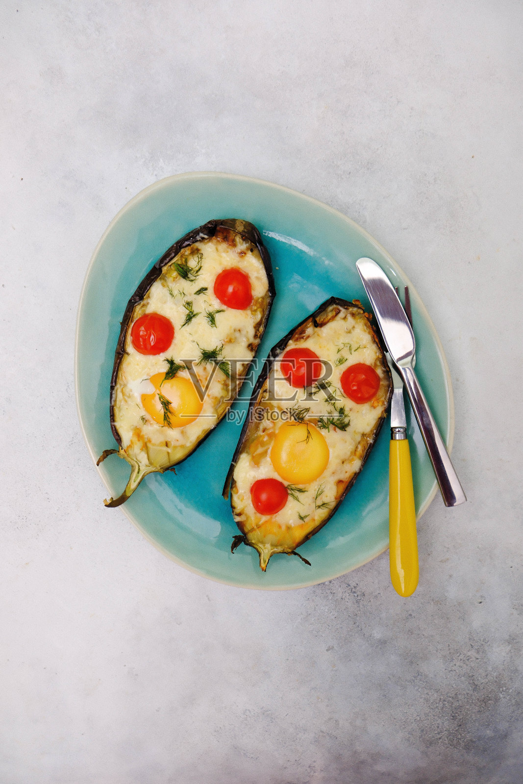 烤茄子,奶酪,鸡蛋和西红柿放在灰色背景的蓝色盘子里。照片摄影图片