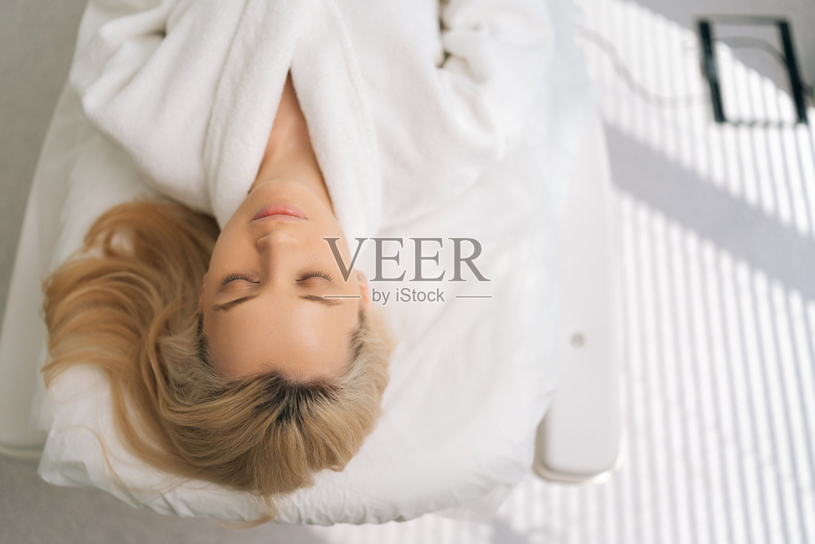 静心的年轻女子,穿着白色浴袍,闭着眼睛躺在医疗沙发上。抗衰老年轻化护肤理念。照片摄影图片