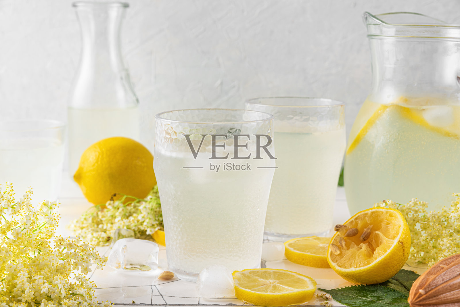 新鲜冰柠檬水,柠檬和接骨木花在一个罐子和杯子在白色瓷砖桌子。照片摄影图片