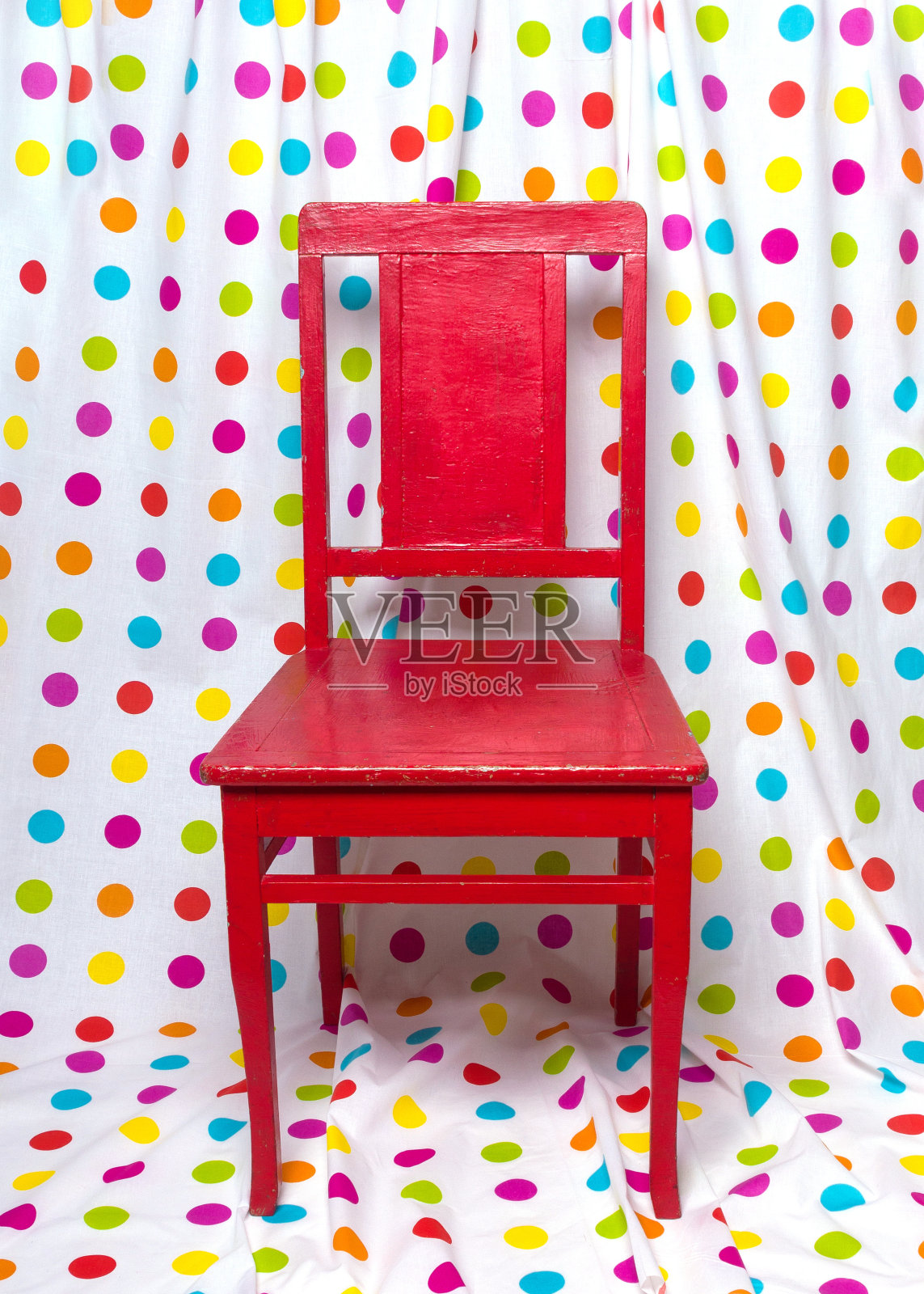 红色的旧椅子,映衬着色彩斑斓的圆点窗帘。照片摄影图片