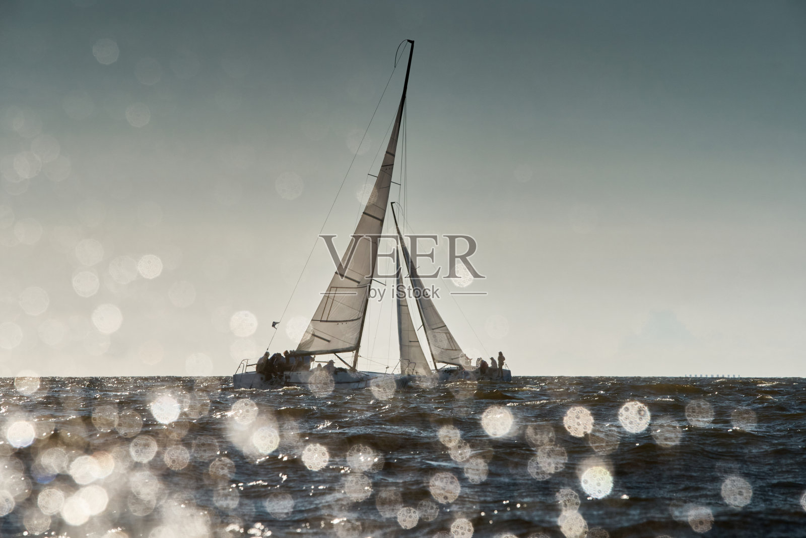 透过浪花看到两艘帆船在日落时如何倾斜,船翻滚,水花在阳光下闪闪发光,甲板上的水手照片摄影图片