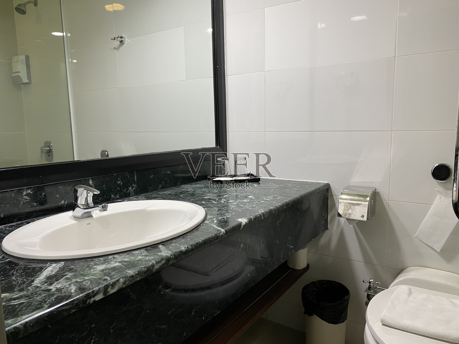 酒店浴室的角落,绿色的瓷砖墙壁,大镜子和白色的脸盆。经典的风格。照片摄影图片