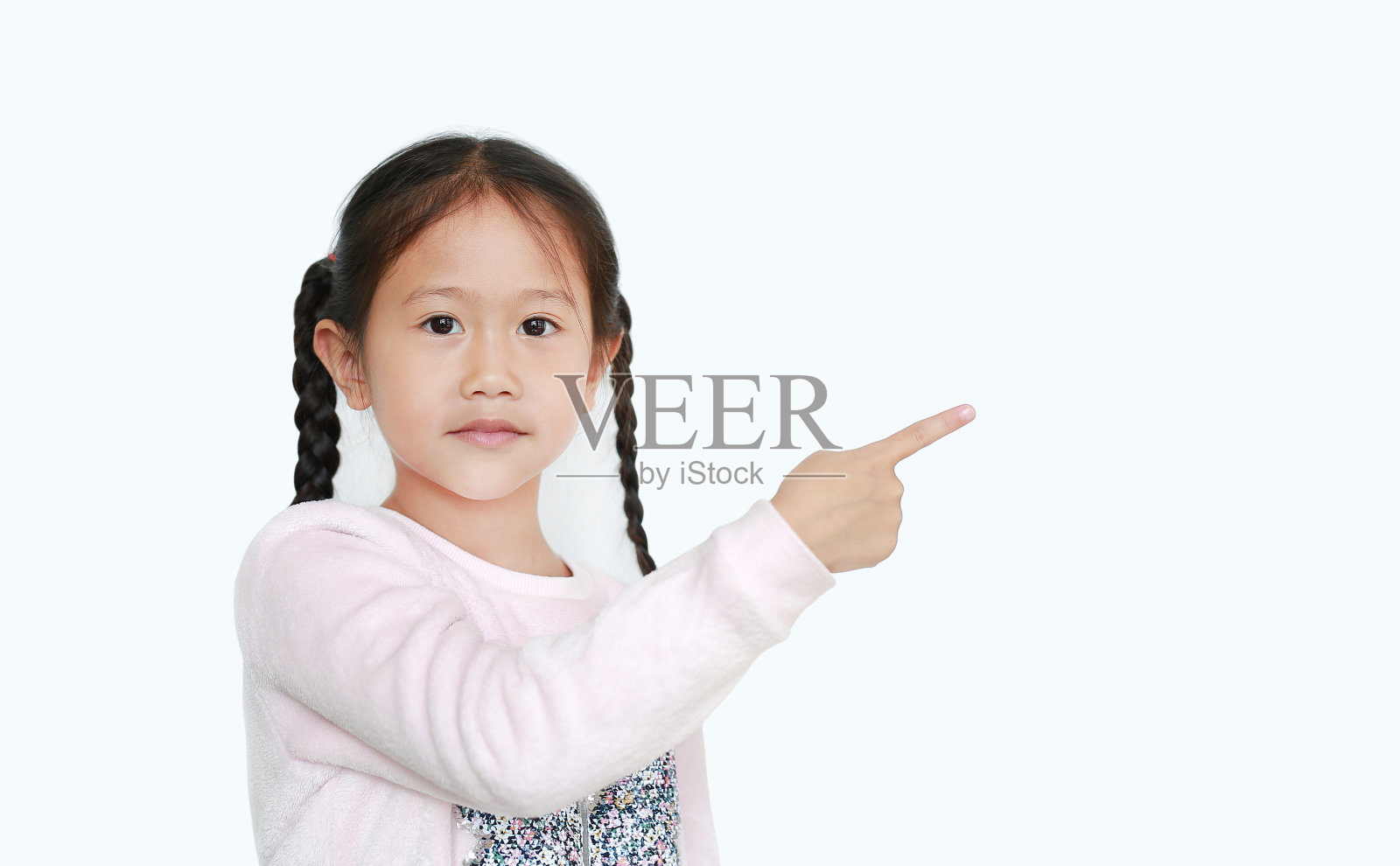开朗的小女孩用食指指着旁边,用空白的白色背景呈现出孤立的东西。教育观念中的亚洲女学生。照片摄影图片