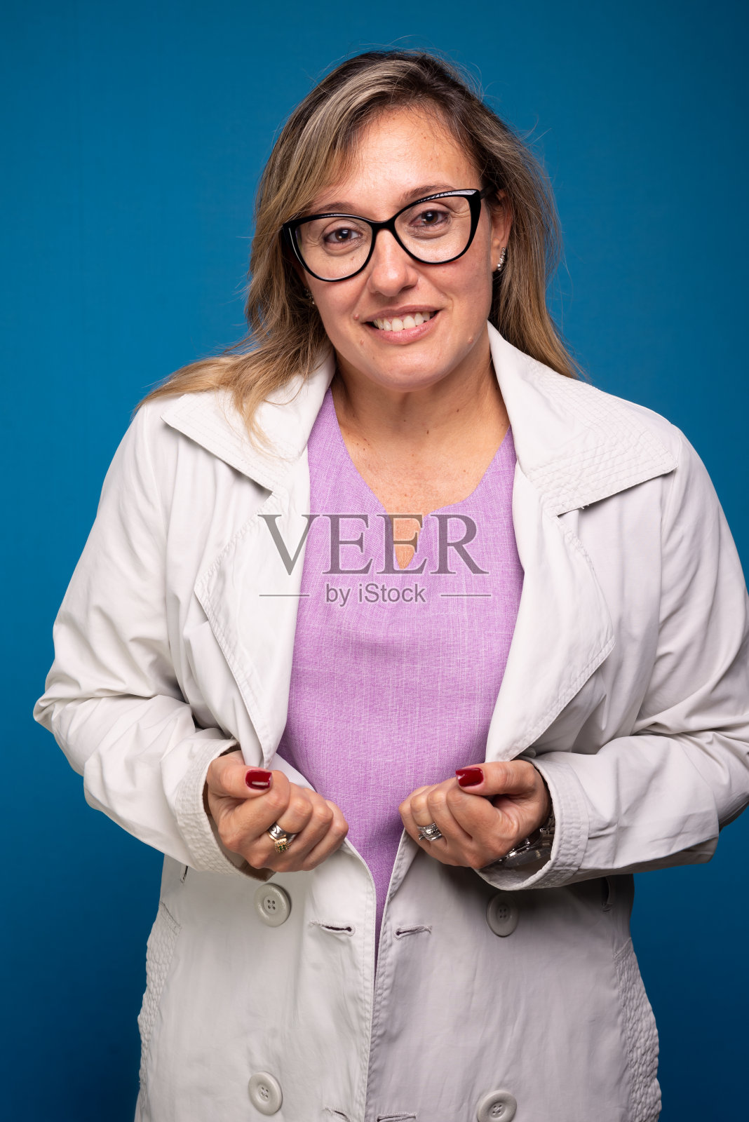 照片中,一位甜美、自信的中年护士穿着白色大褂和淡紫色上衣,戴着眼镜看着镜头。照片摄影图片