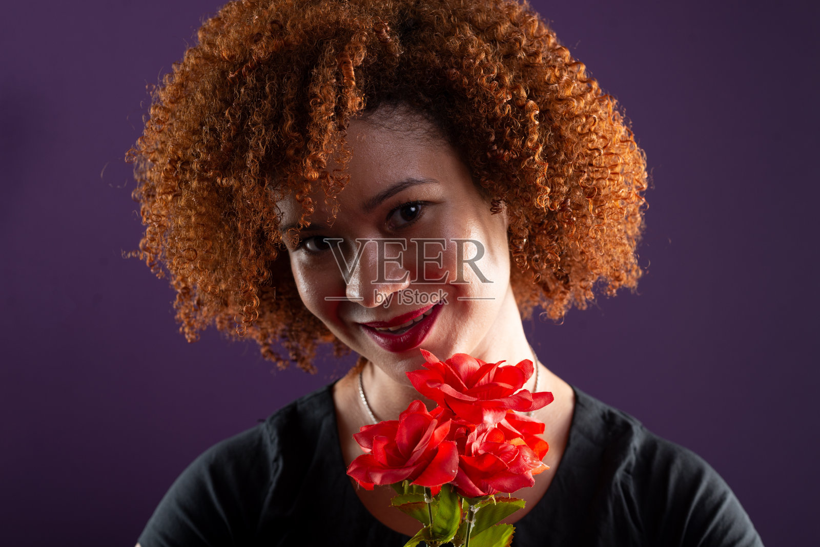 一个有着红色卷发的美丽女人的特写肖像,她的脸上拿着一朵红色的花。照片摄影图片