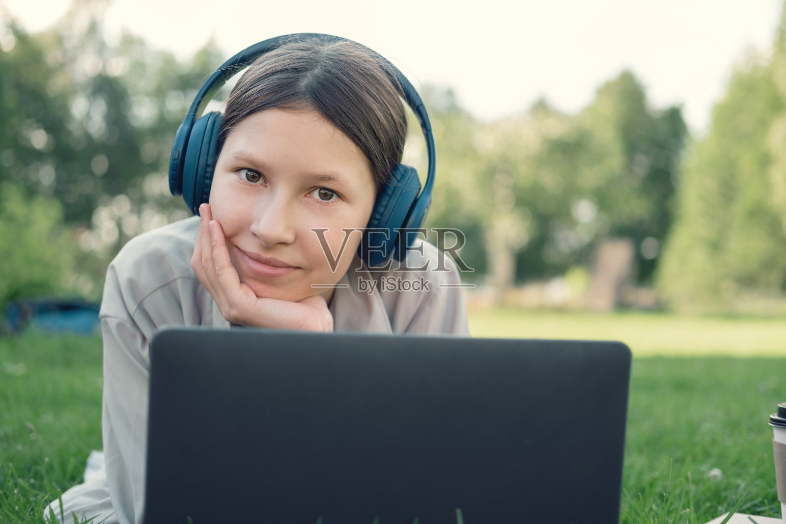 十几岁的女学生坐在户外读书,看她的书,平板电脑和笔记本。回到学校。在校园里或公园里,女学生躺在草地上使用笔记本电脑。远程学习。照片摄影图片