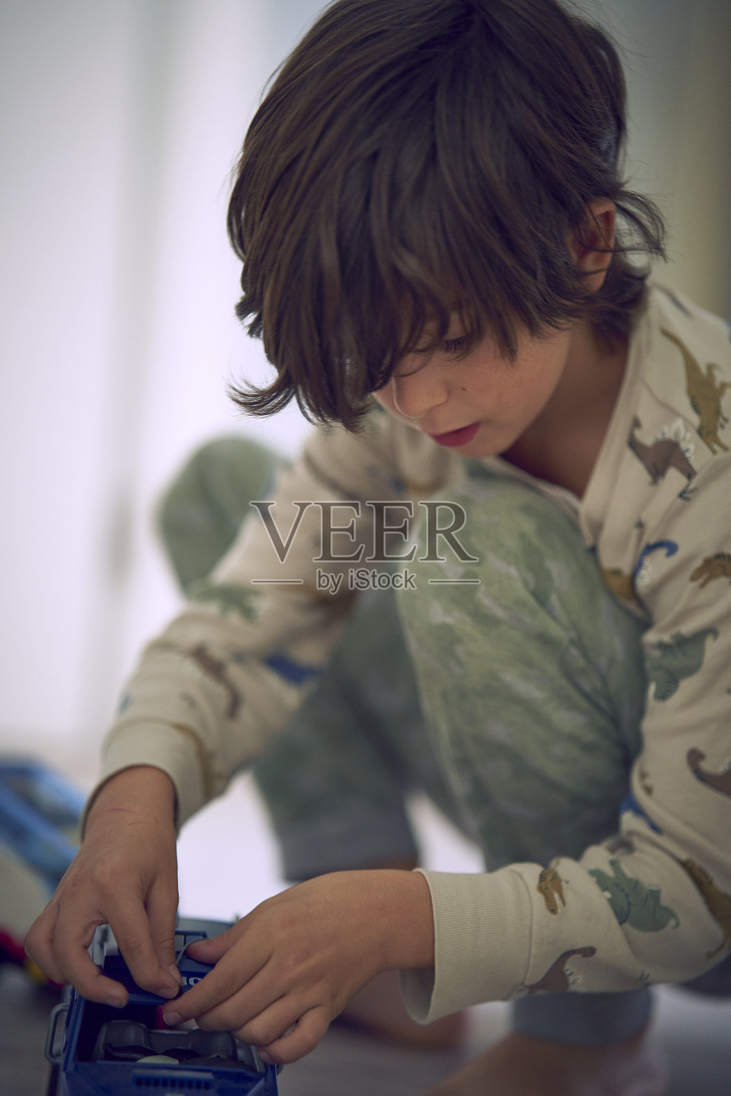 刚起床的男孩,披头散发,兴奋地弯着腰,拿着圣诞礼物,骑着警车的警笛。照片摄影图片