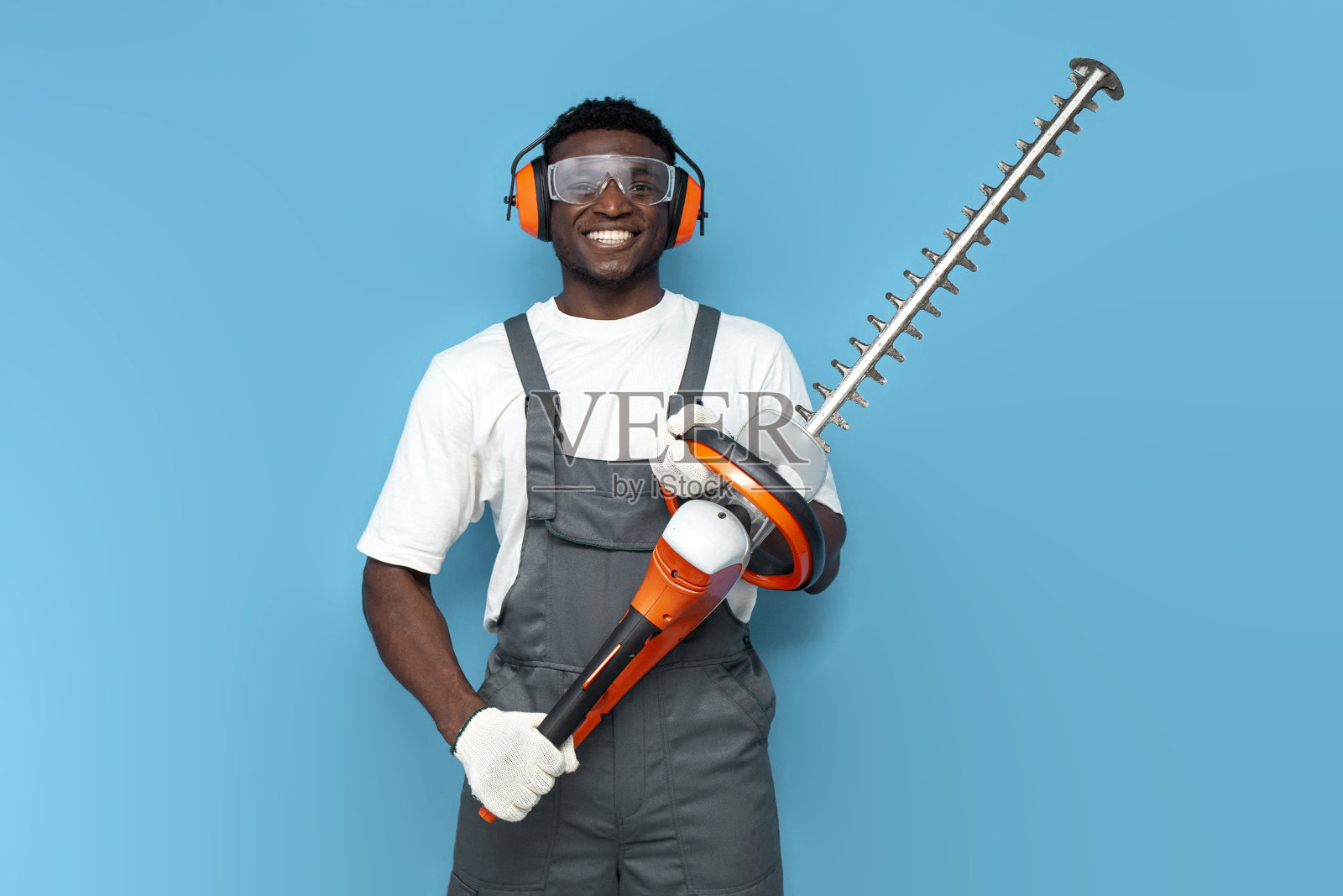 穿着制服的园艺工人手持电刷切割器在蓝色孤立的背景上照片摄影图片