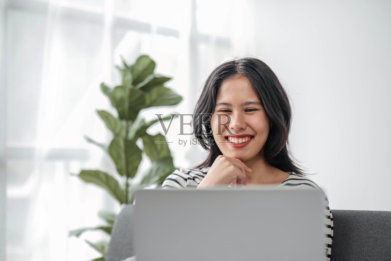 年轻的商业自由亚洲女性工作在笔记本电脑上查看社交媒体,躺在沙发上,放松在家里的客厅。照片摄影图片