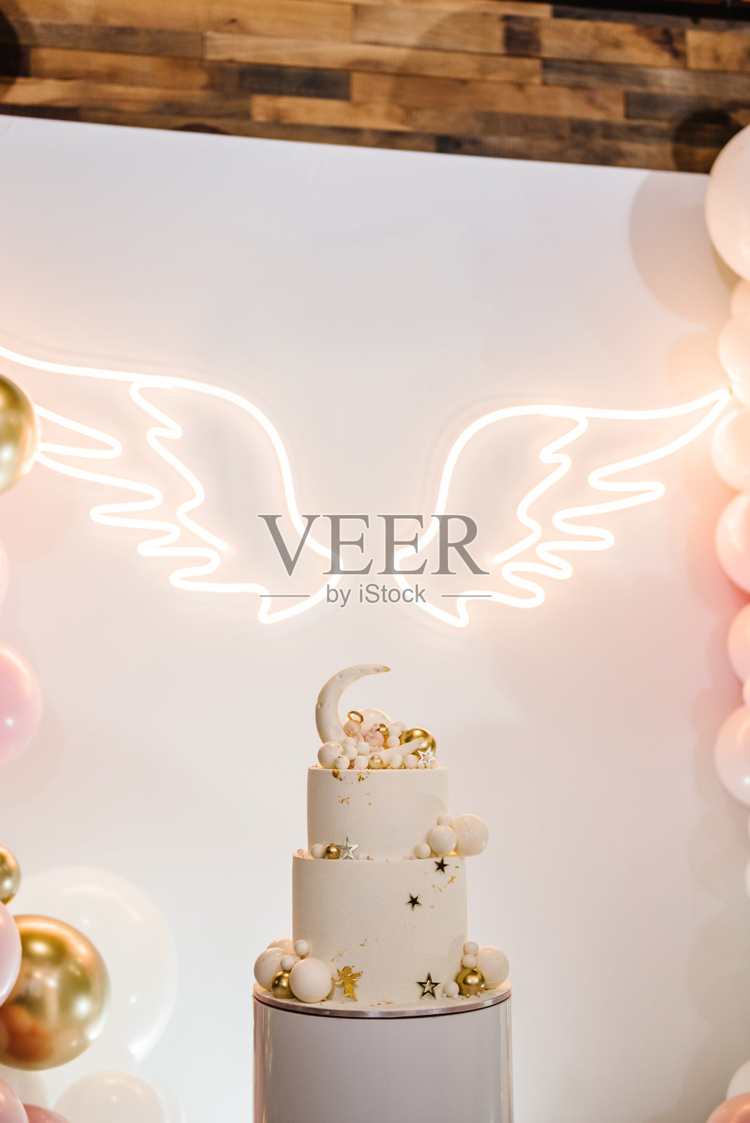 装饰时髦的蛋糕。庆祝洗礼的概念。拱门上装饰着粉色、白色、金色的气球,天使的翅膀。宝宝生日派对的接待处挂在墙上。在拍照区,区域有美味的接待。照片摄影图片