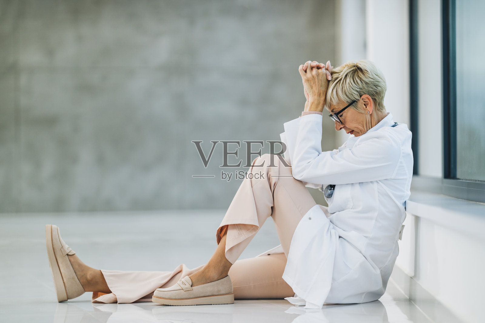 在空无一人的医院走廊里,一位疲惫的女医生在短暂的休息时间显得忧心忡忡照片摄影图片