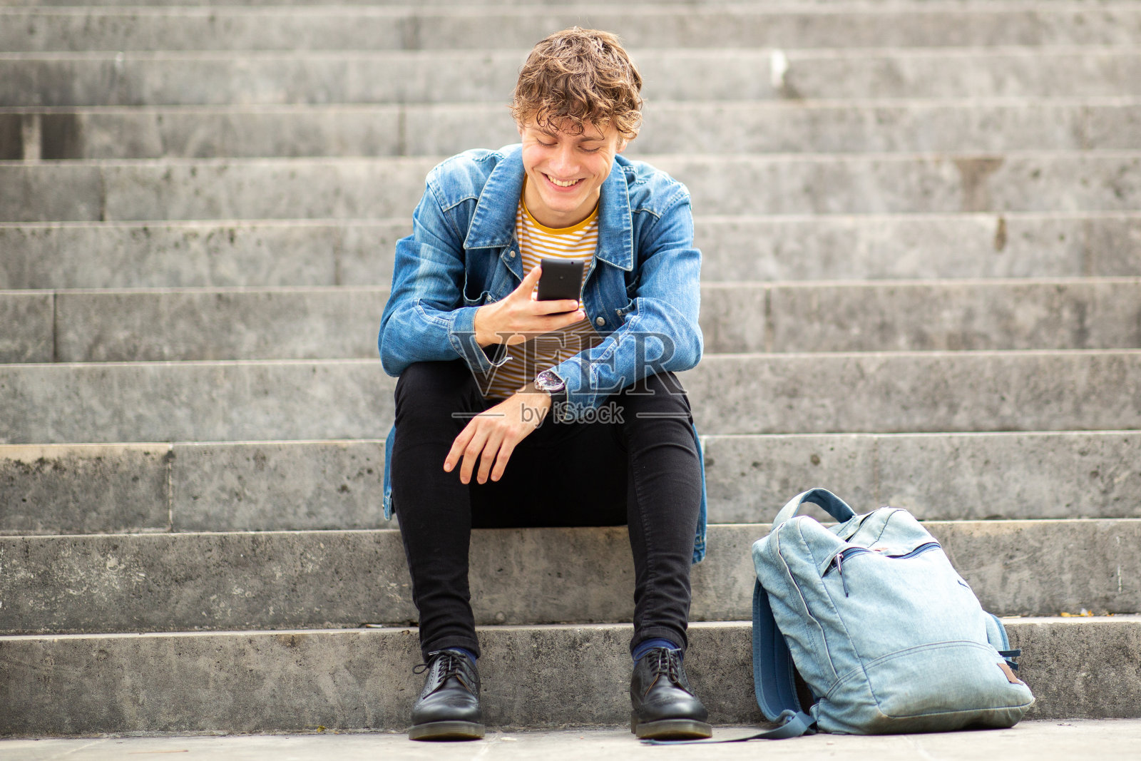 一个面带微笑的年轻人坐在外面的台阶上玩手机照片摄影图片
