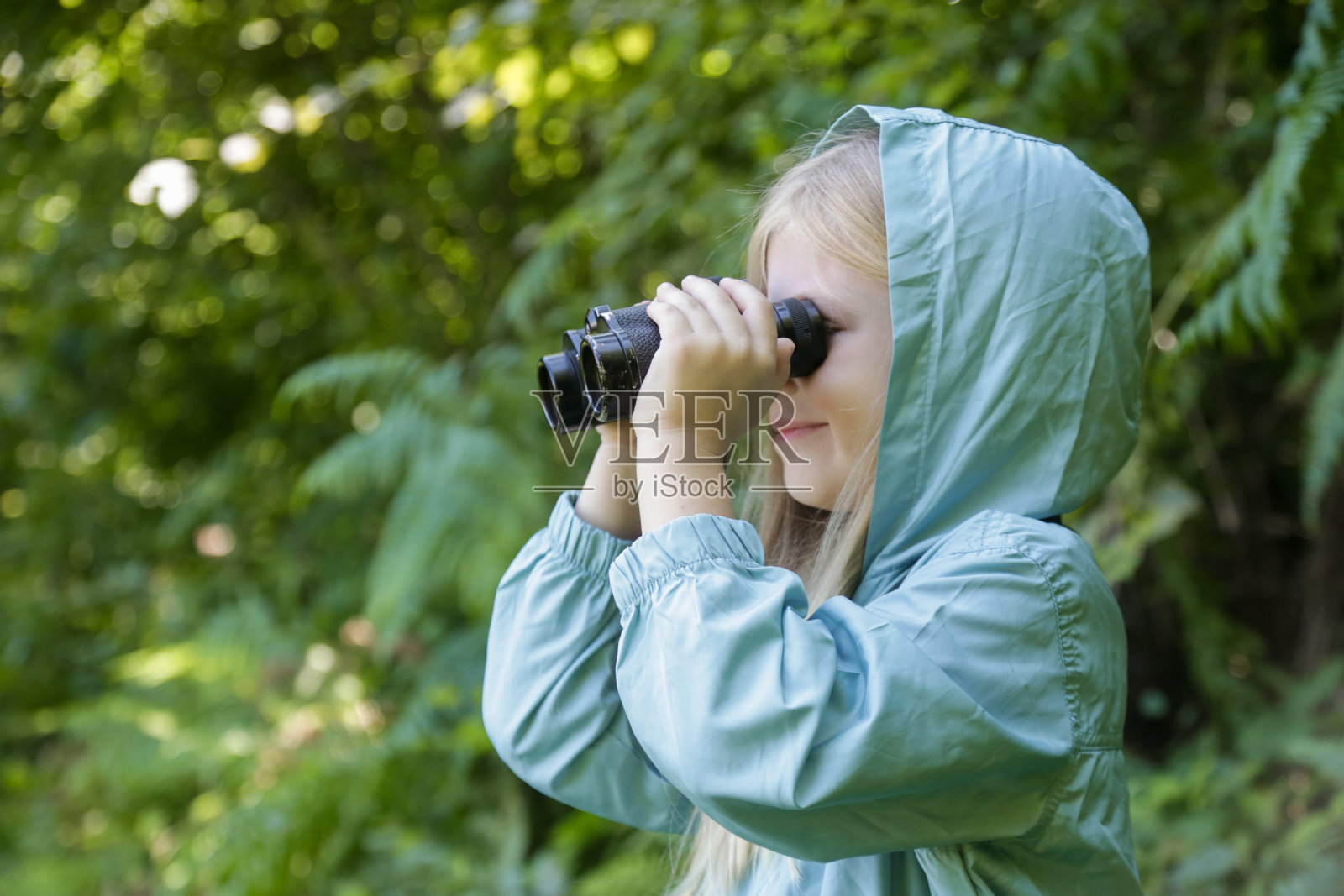 可爱的小女孩通过双筒望远镜探索大自然。孩子在户外玩耍。儿童旅行,冒险和观鸟的概念。照片摄影图片