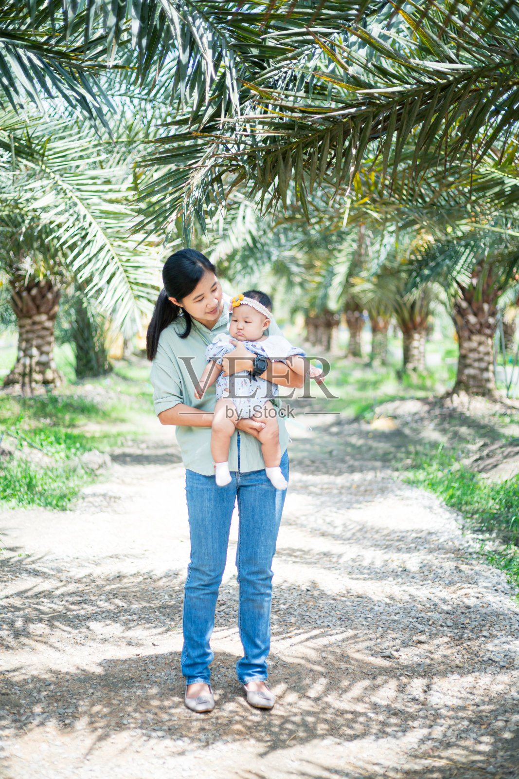亚洲女人抱着一个婴儿,母亲抱着她的孩子,亚洲年轻美丽的母亲抱着她的新生儿正在睡觉,感受着爱和温柔的触摸,然后坐在公园的绿草地上照片摄影图片