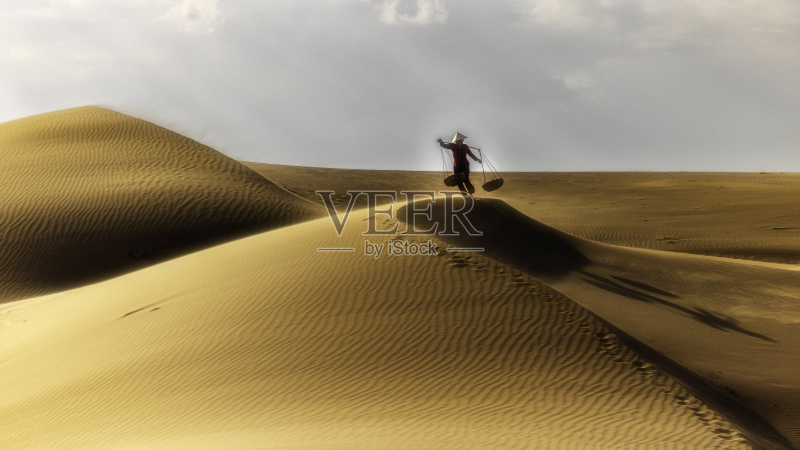 在越南南部的潘令省,一名妇女穿着便服,头戴圆锥形帽子,走在南广的沙丘上。照片摄影图片