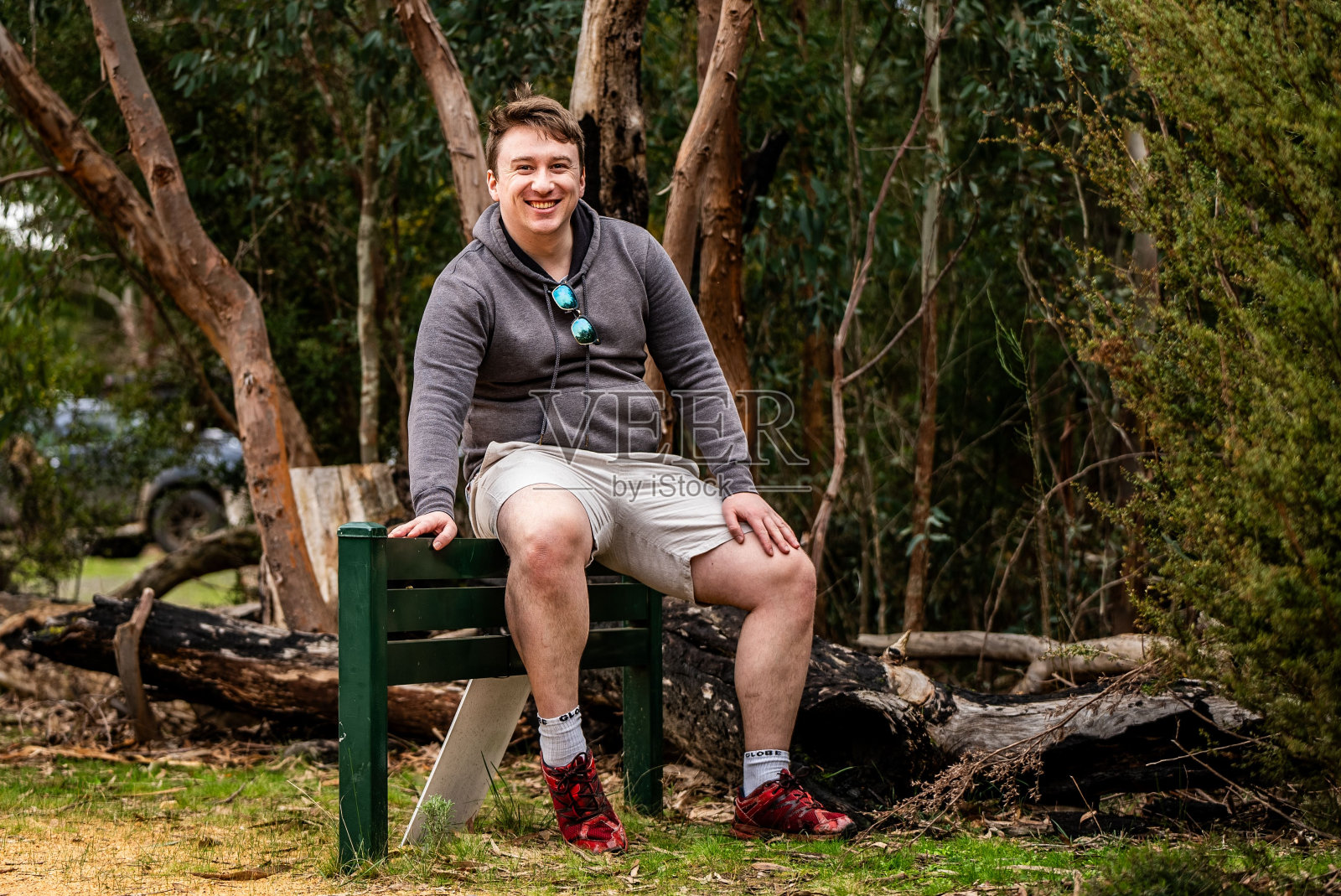 一名白人男子坐在公园的绿色长椅上,周围是一片宁静的树林。照片摄影图片