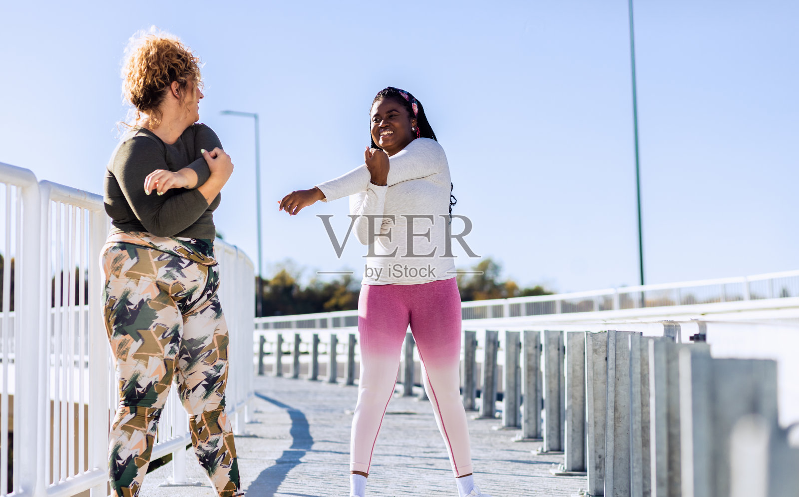 两个大码的年轻女人在跑步前一起做伸展运动。照片摄影图片
