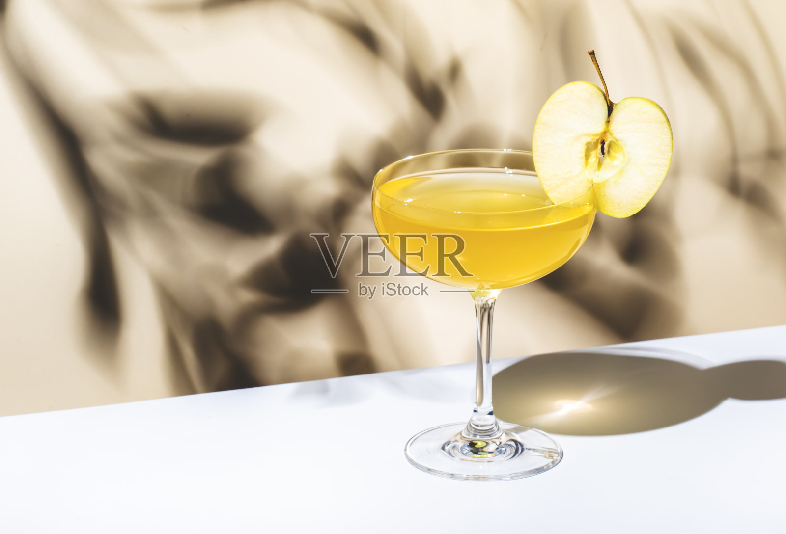 苹果派鸡尾酒,搭配伏特加、苹果利口酒和肉桂糖浆。浅米色背景,硬光,阴影图案照片摄影图片