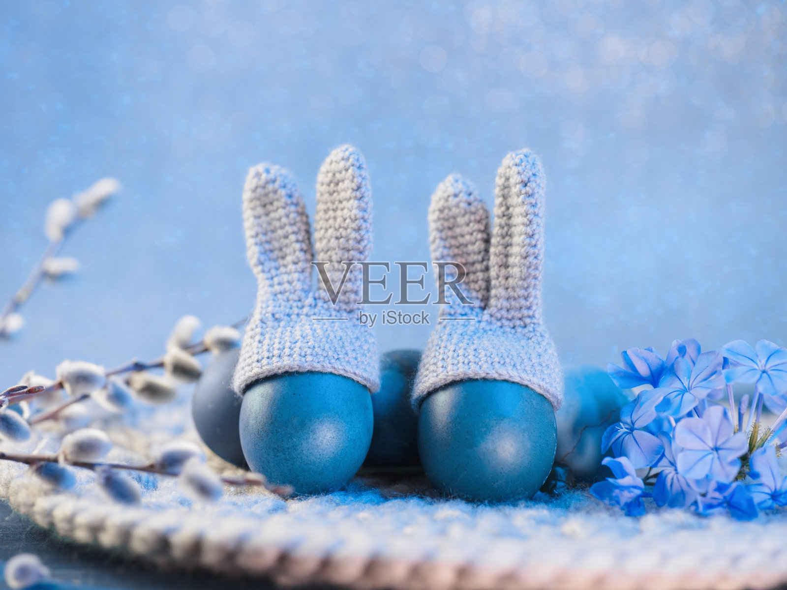 桌上有蓝色的复活节彩蛋,帽子上有兔子耳朵,餐巾上织着。蓝色背景照片摄影图片