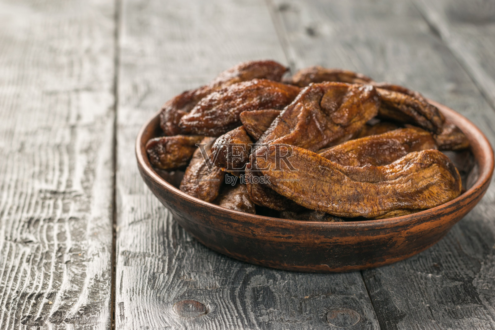 黑木桌上,瓷碗里的干香蕉。照片摄影图片