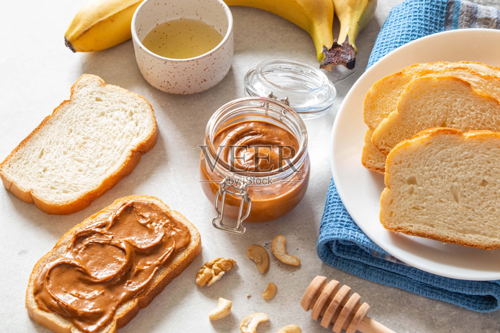 果仁黄油吐司配香蕉和蜂蜜放在轻桌上。核桃,榛子和腰果铺在玻璃罐里。自制早餐三明治。健康食品的概念。照片摄影图片