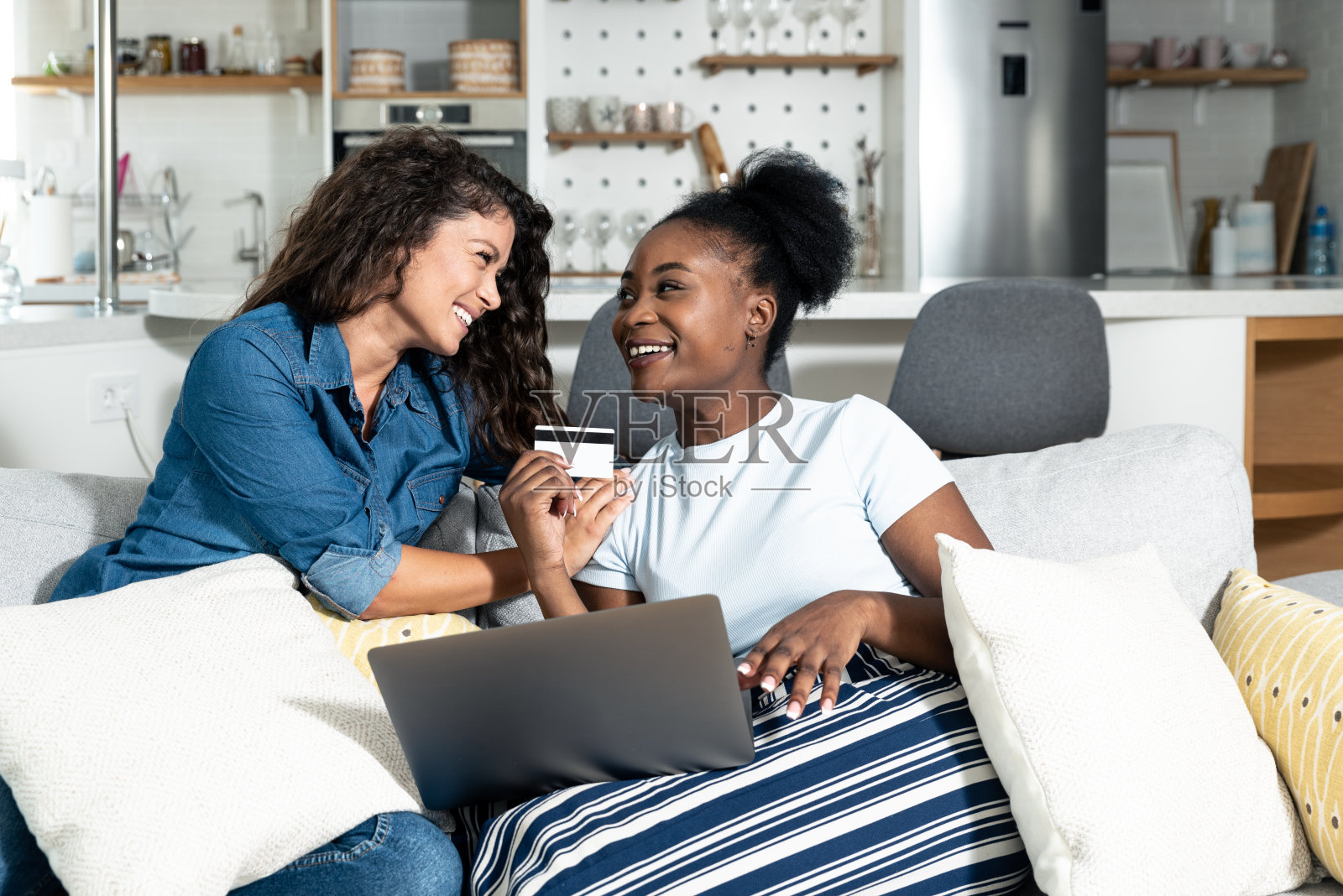 两个无忧无虑的年轻女性生意伙伴和老板,坐在沙发上的朋友们很高兴,因为他们刚刚尝试用信用卡在他们新的网上商店网站上购物。照片摄影图片