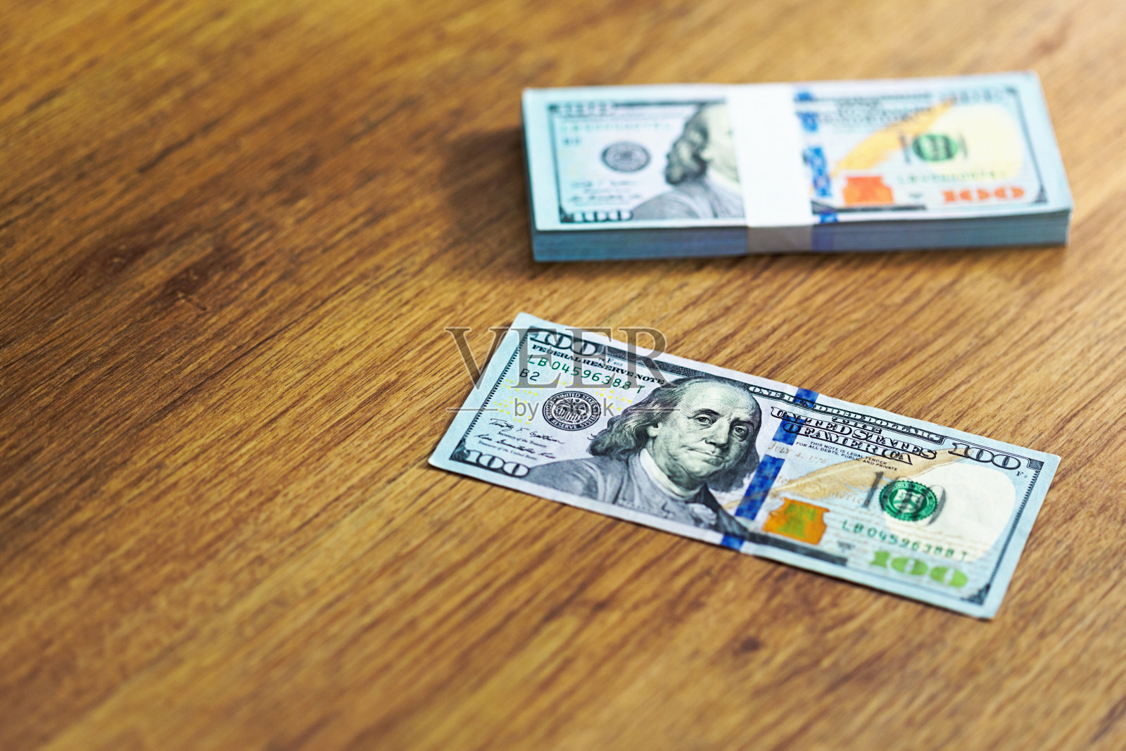 100美元的钞票散落在木质表面上,其中包括一捆用货币带包裹的钞票照片摄影图片