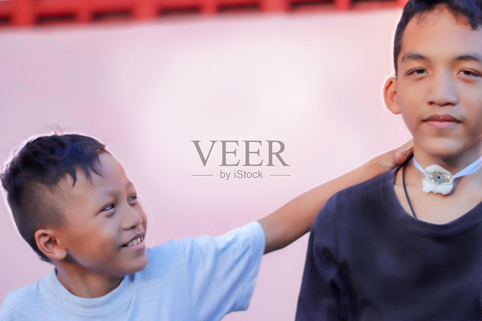 亚洲男孩,他和他的兄弟生病了,他正在通过一个清晰的喉管呼吸,背景是抽象的粉红色,但他看起来像是在微笑,对生活很满意。照片摄影图片