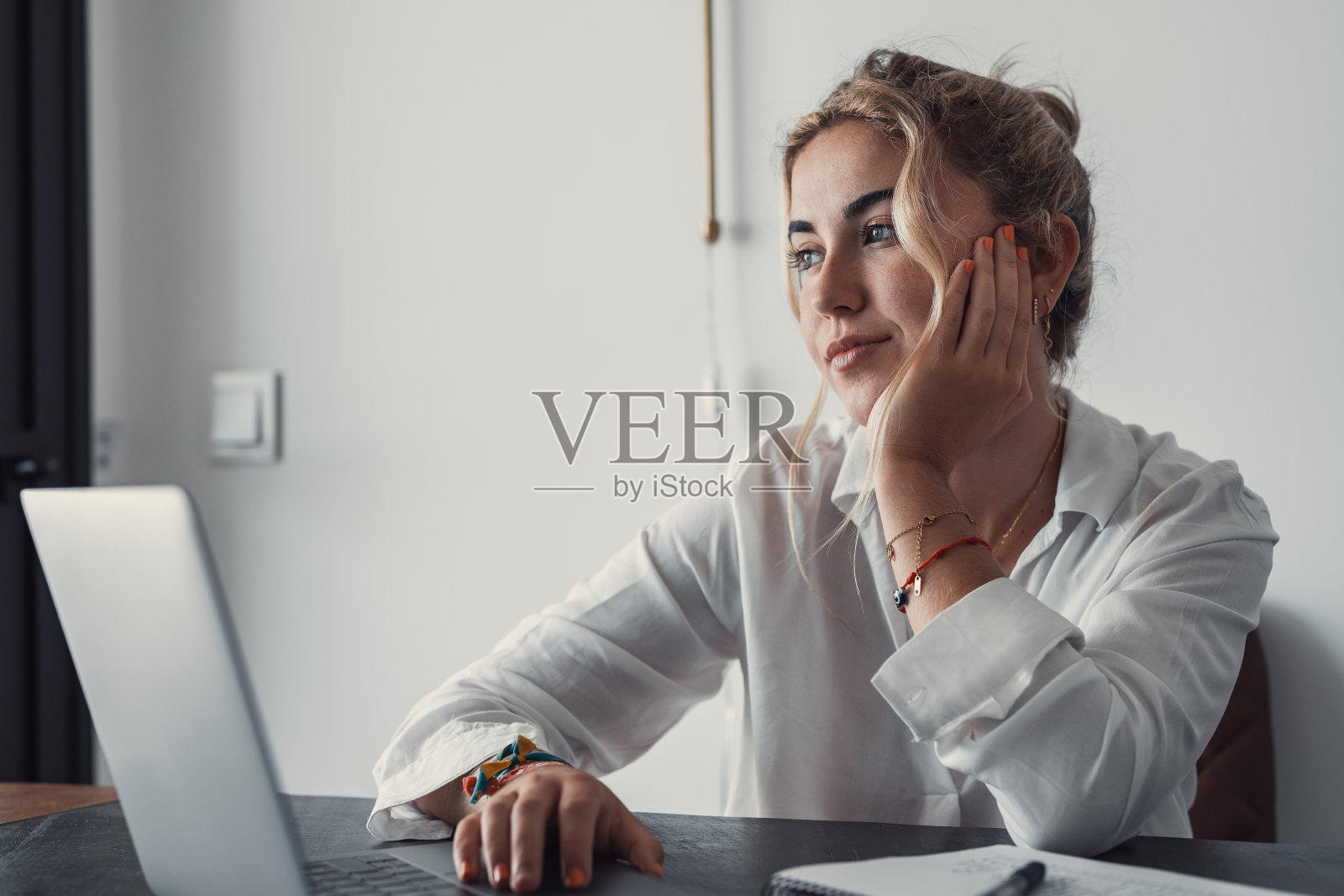 有思想的千禧一代女学生坐在桌子旁,拿着笔记本电脑,打开书,看向别处,思考培训课程,学习网络研讨会,在线课程,测试。网上学习,在家远程办公照片摄影图片