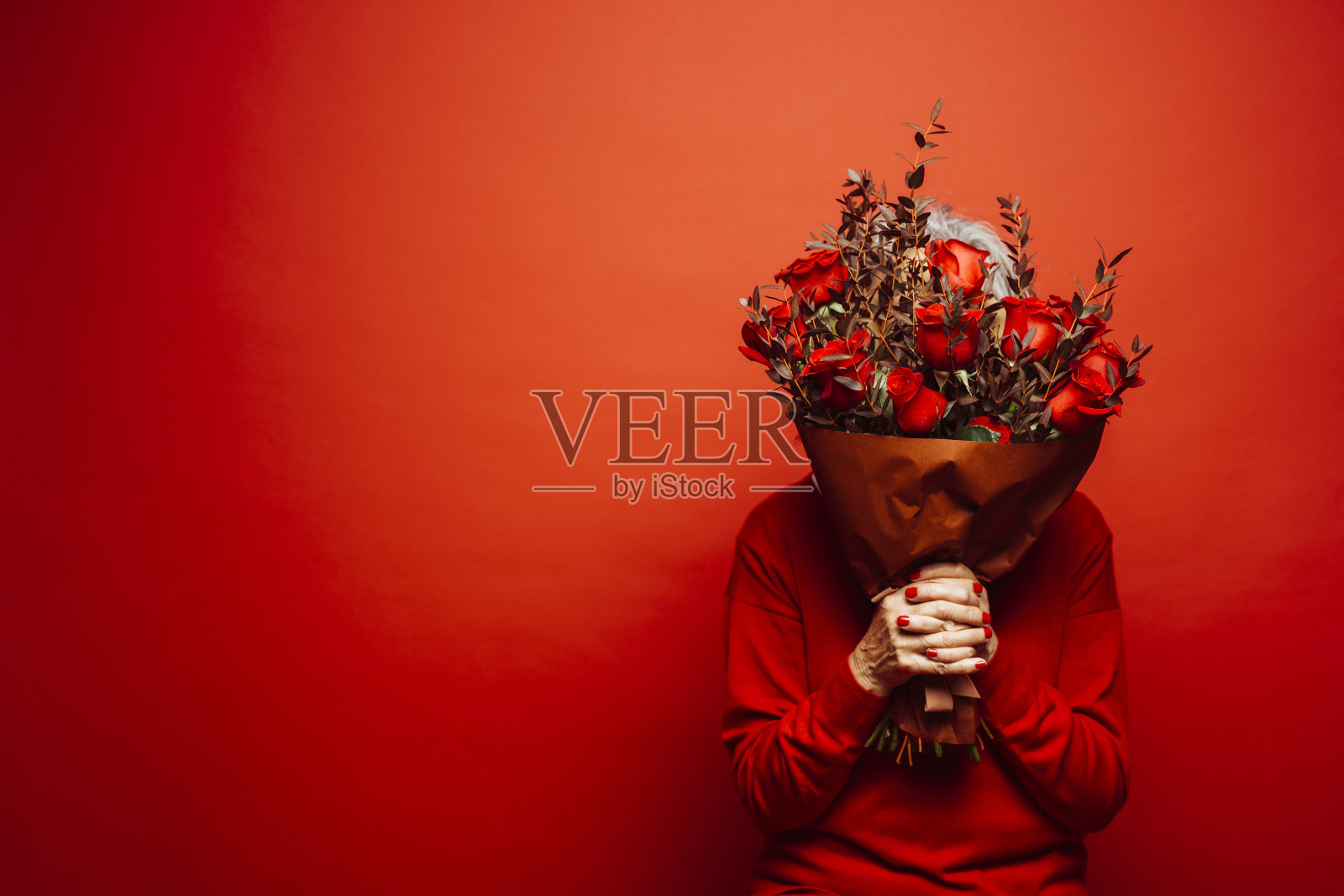 匿名女子手持一束红玫瑰,前面是红色背景照片摄影图片