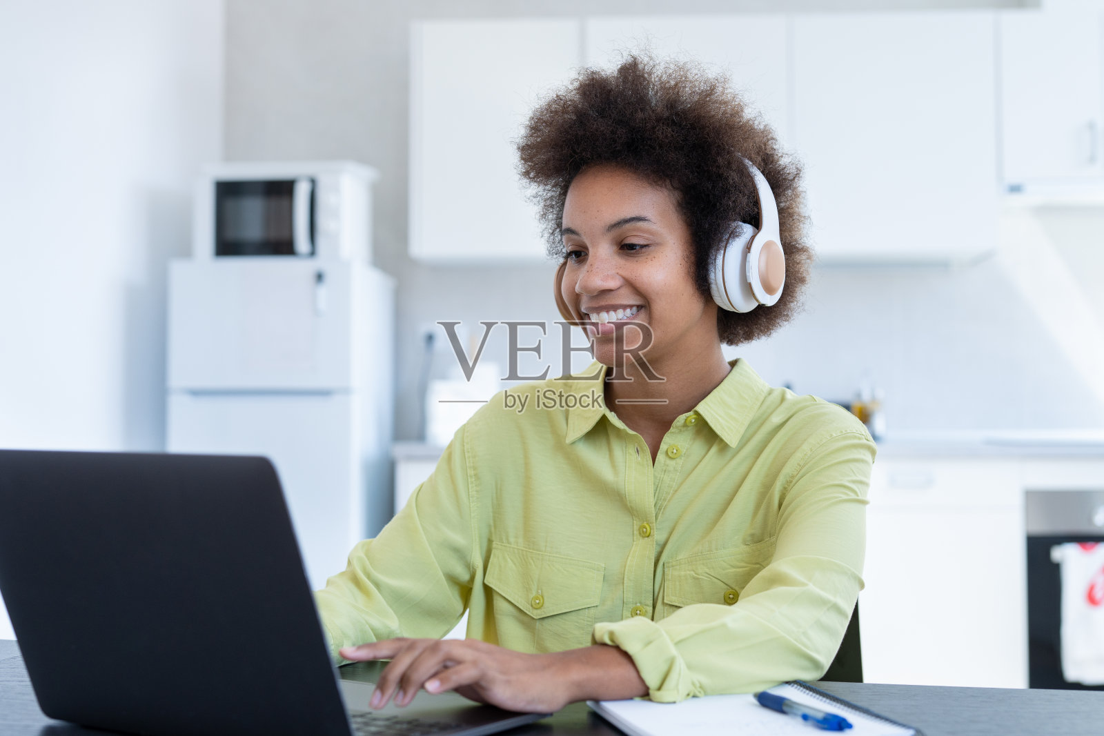 快乐放松的千禧一代美国黑人女商人戴着无线耳机在工作场所休息完成工作,听音乐播客,感受心灵的平静概念坐在办公桌前在阳光明媚的办公室照片摄影图片