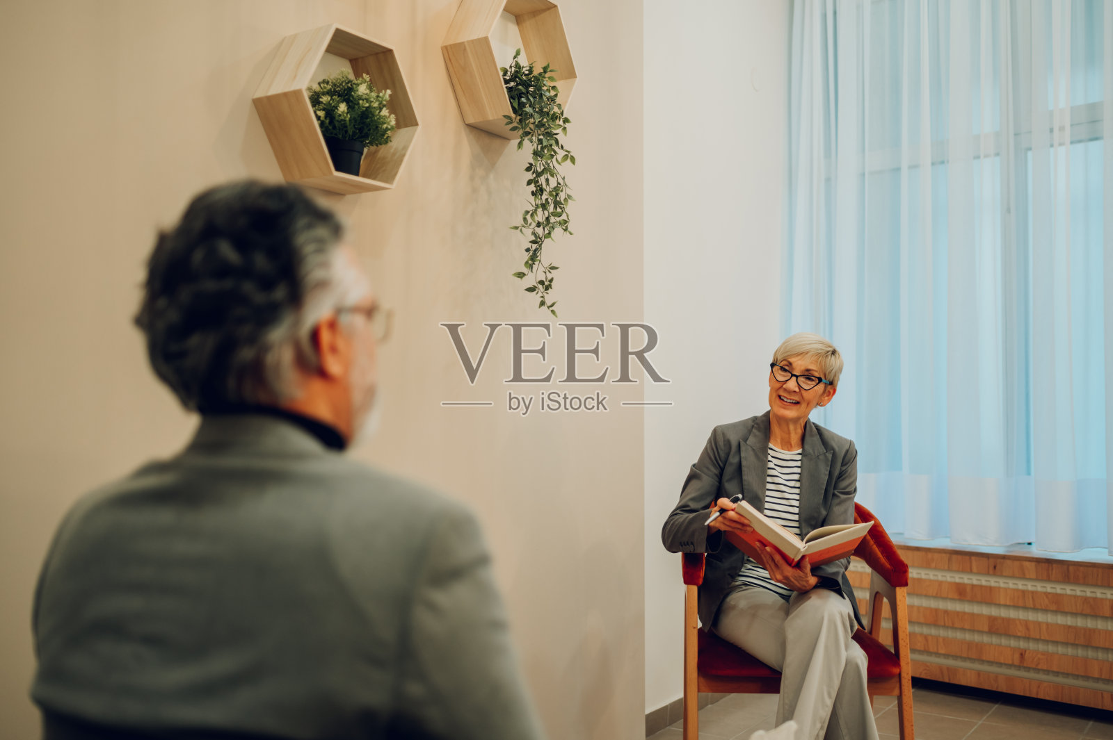 一位快乐的心理治疗师正坐在那里,手里拿着一本教科书,与客户讨论进展。照片摄影图片