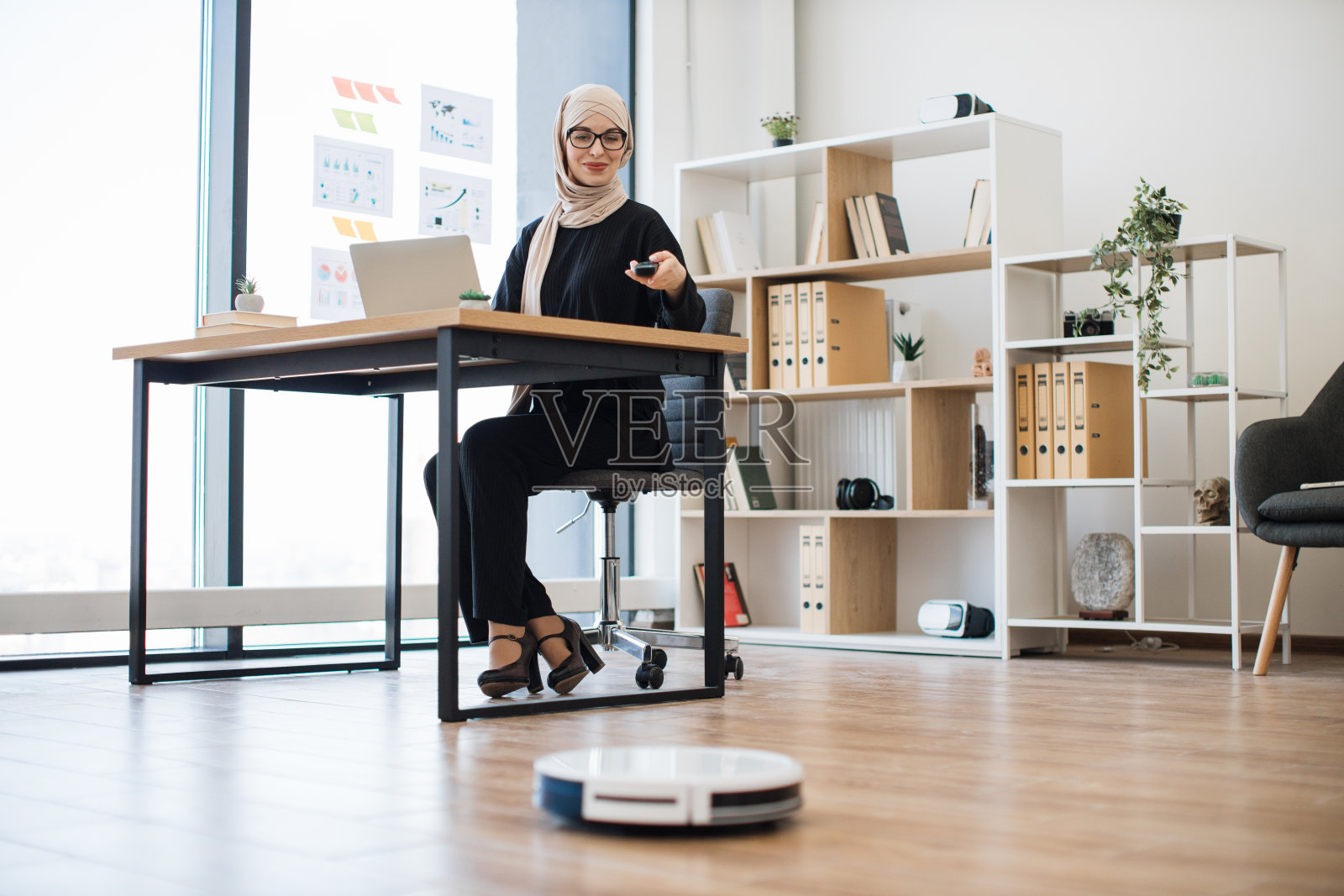 一名妇女在工作时通过遥控器打开机器人吸尘器照片摄影图片