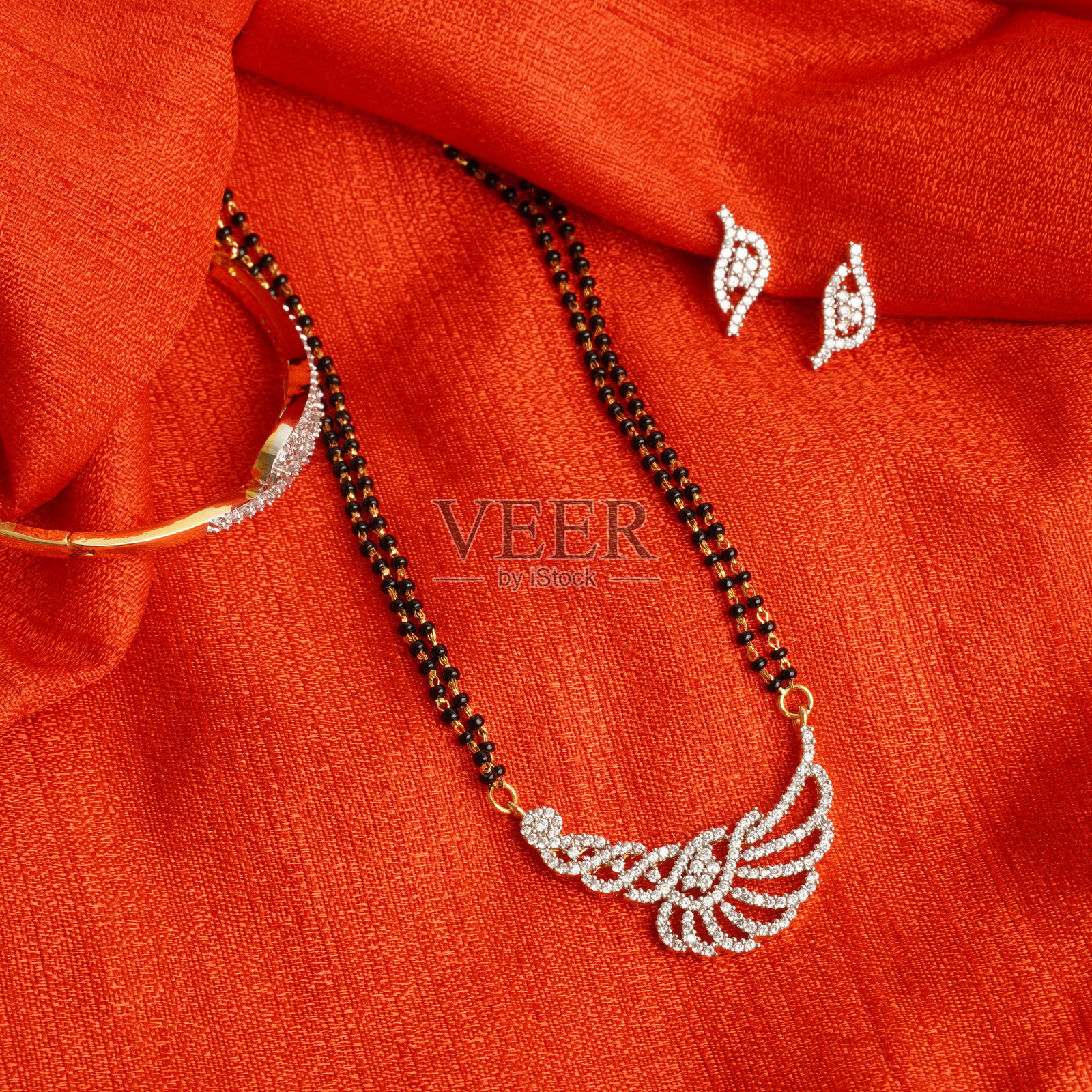 一套钻石吊坠在金链与黑色和金色的珠子,钻石耳环和钻石手镯。点击闪亮的红色织物背景。照片摄影图片