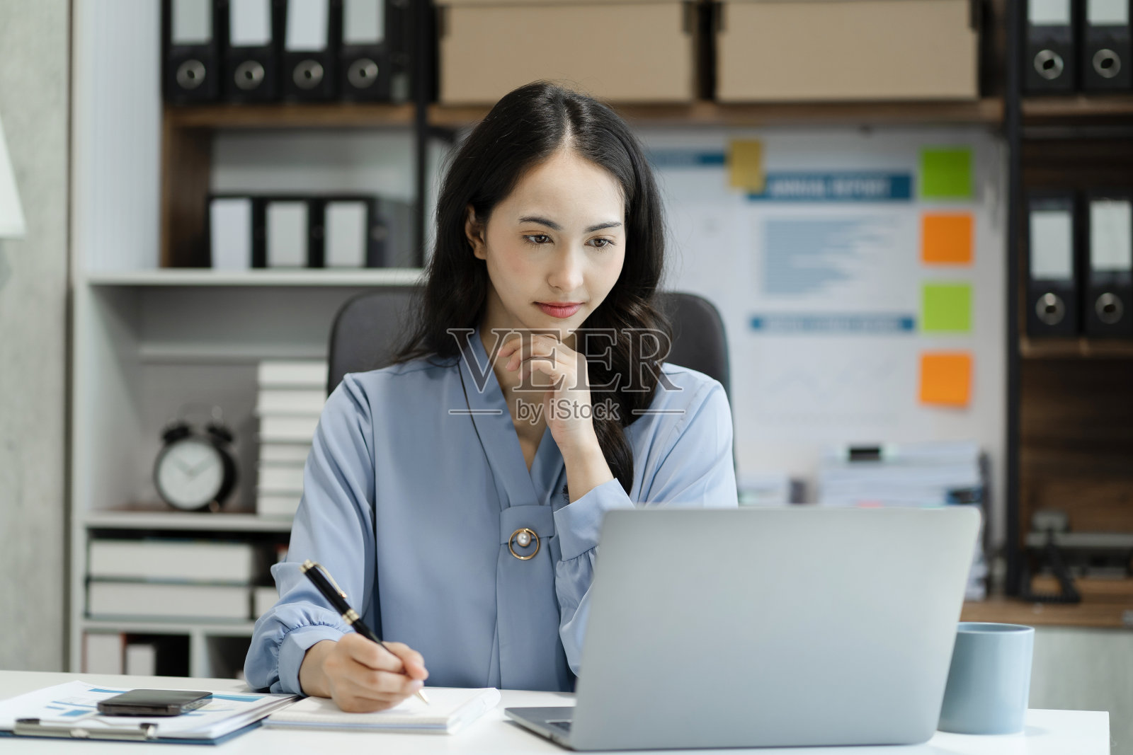 商务女性在办公室里用手在平板电脑、电脑和笔记本上写字。木桌上有一张商业图表。照片摄影图片