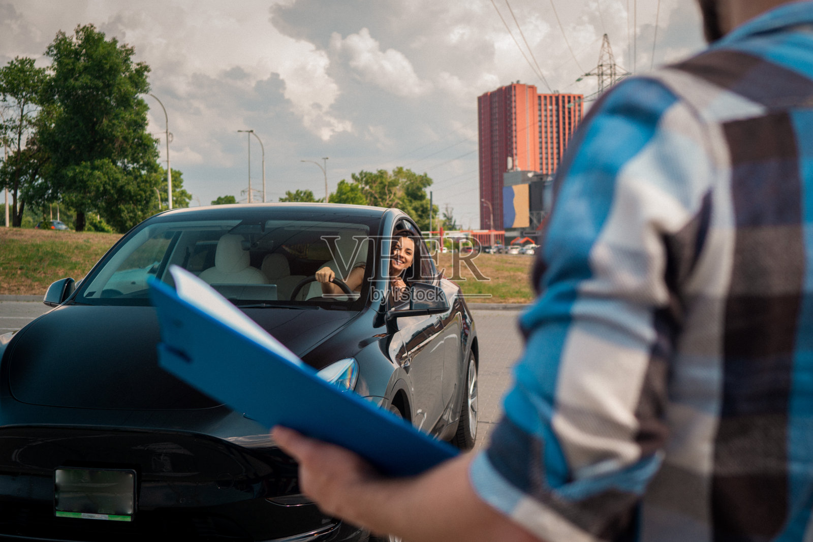 微笑着学开车的女人看着窗外,看着拿着测试报告的教官。驾驶考试,驾驶课程,考试概念照片摄影图片