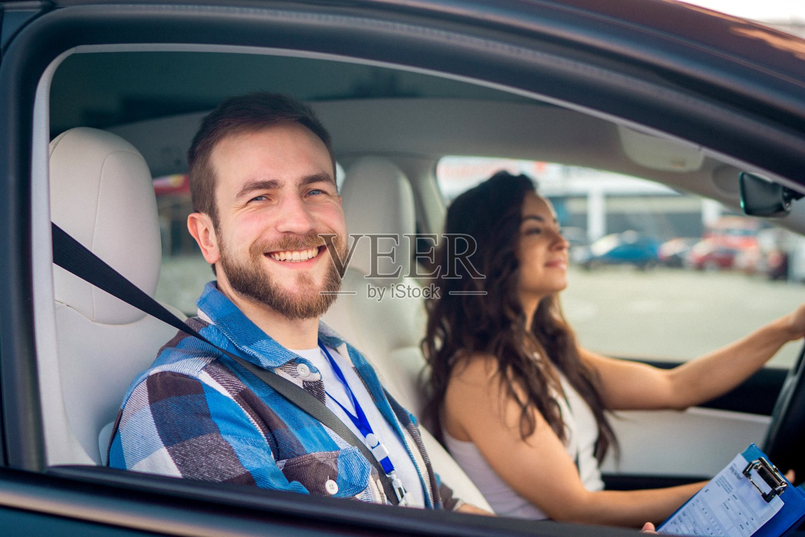 快乐的男教练拿着检查表坐在副驾驶座位上,而女士在驾驶考试中开车。驾驶考试,驾驶课程,考试概念照片摄影图片