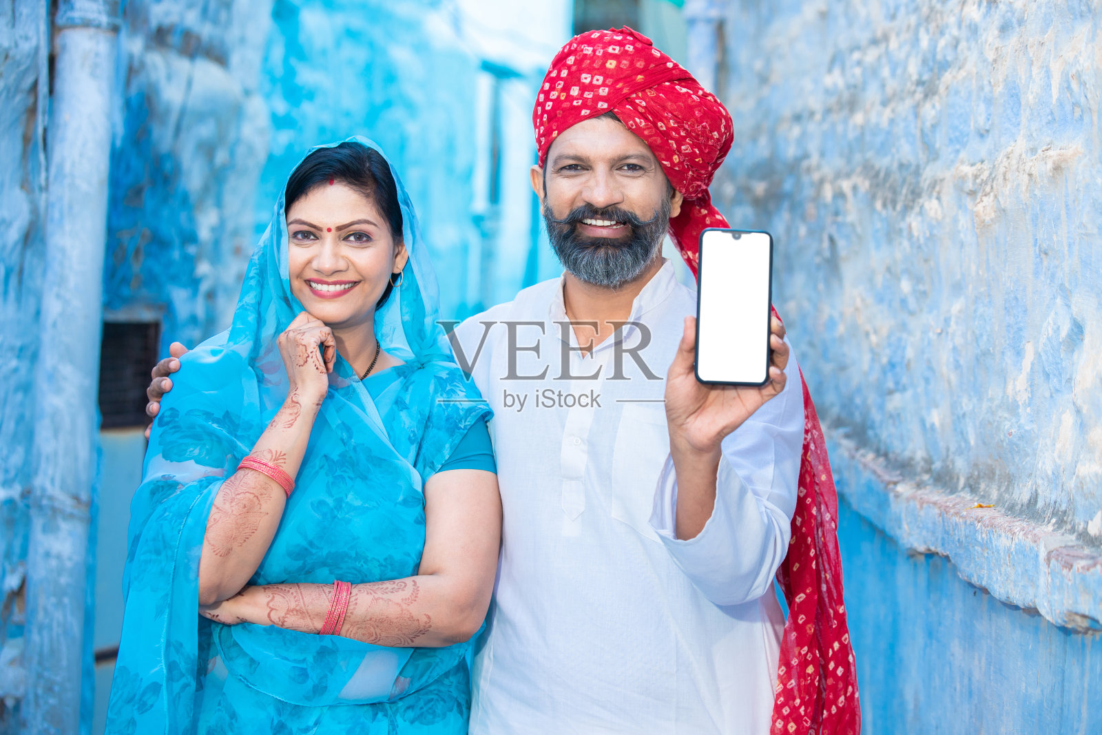 传统的印度夫妇展示空白的智能手机屏幕,戴着红色头巾的男人和穿着纱丽的女人拿着空白的手机显示屏,用于广告和品牌宣传。照片摄影图片