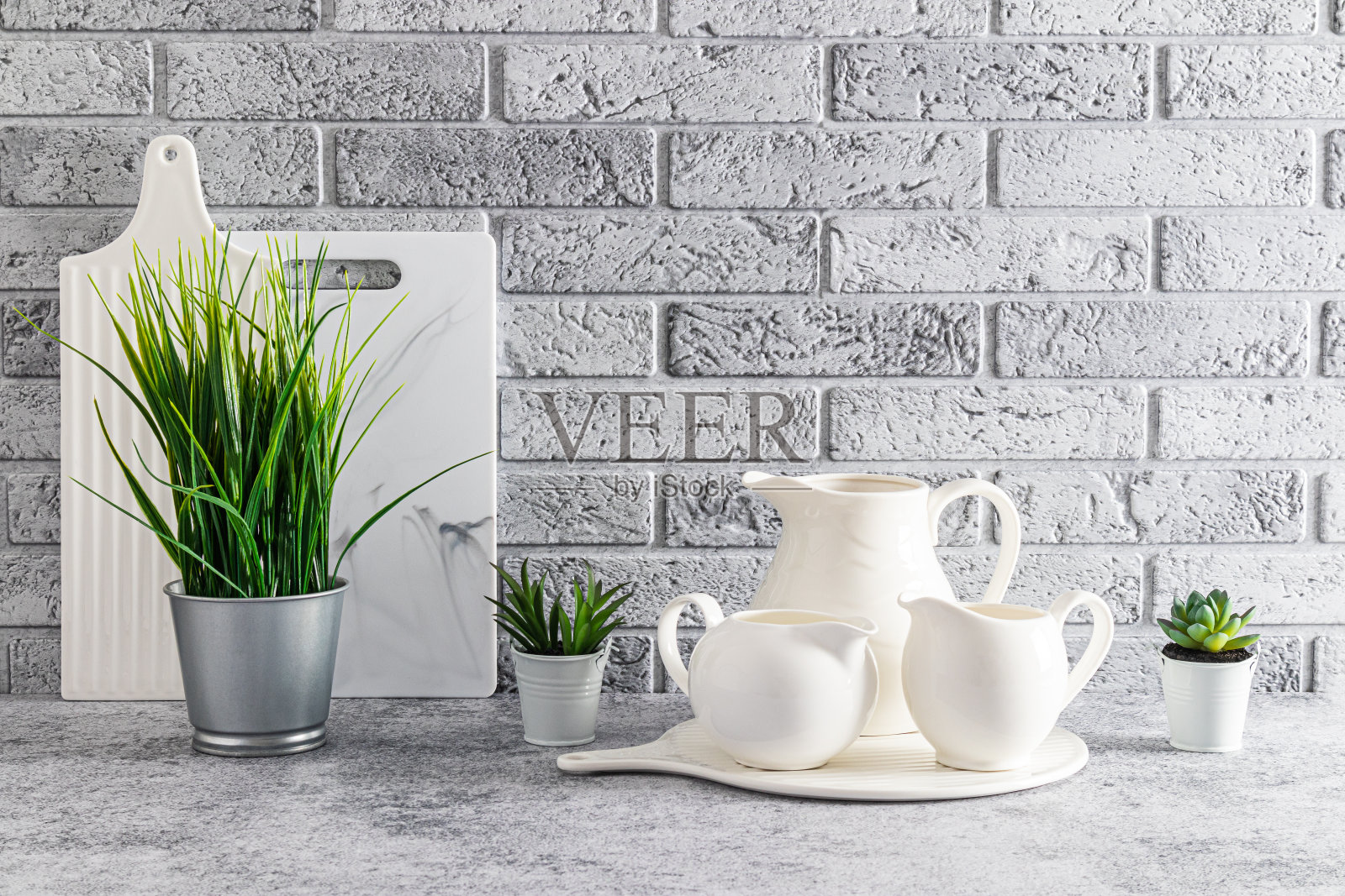 美丽时尚的厨房背景在浅色。灰色的石头台面上摆放着一套白色水壶、砧板和室内植物。灰色砖墙。照片摄影图片