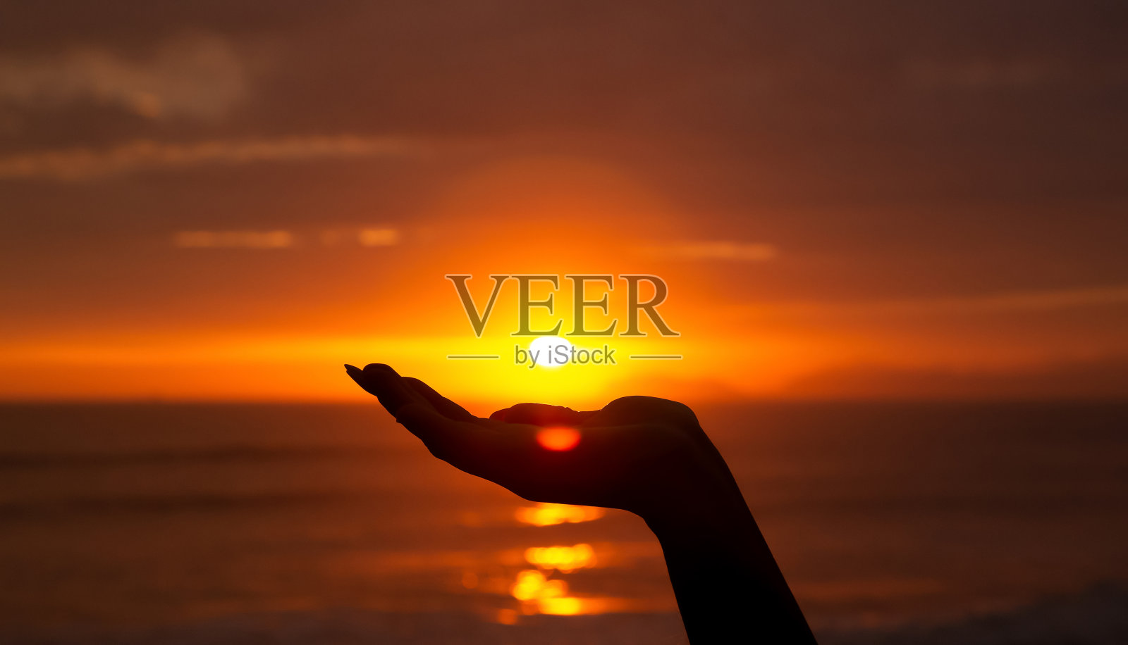 一只手握着太阳的剪影,在夕阳的海面前。日光。文本空间照片摄影图片