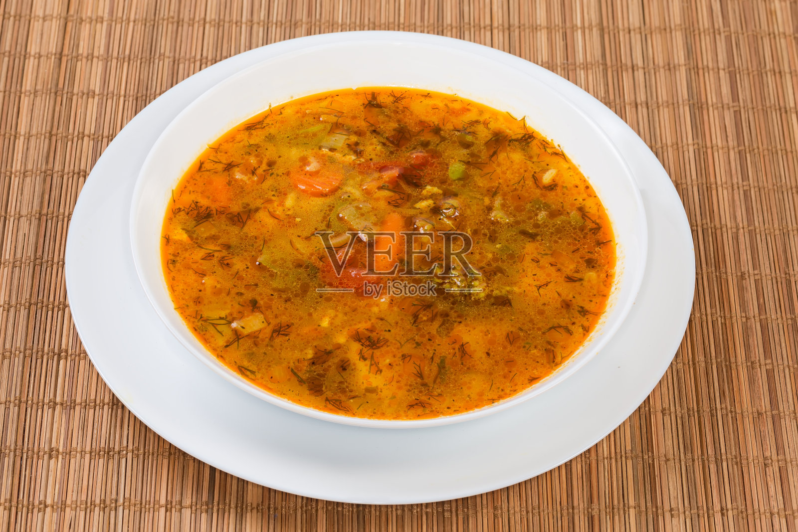 青菜红汤盛在竹制餐具垫上的碗里照片摄影图片