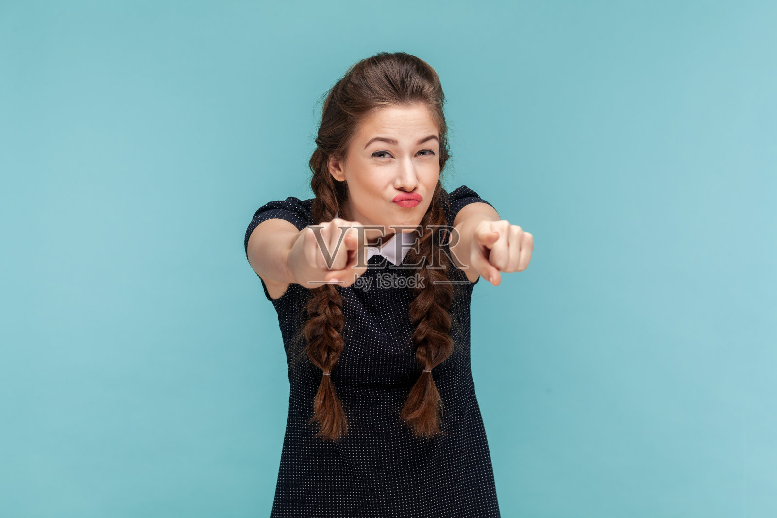有趣迷人的年轻女子,扎着辫子指着你,皱着眉头看着镜头。照片摄影图片