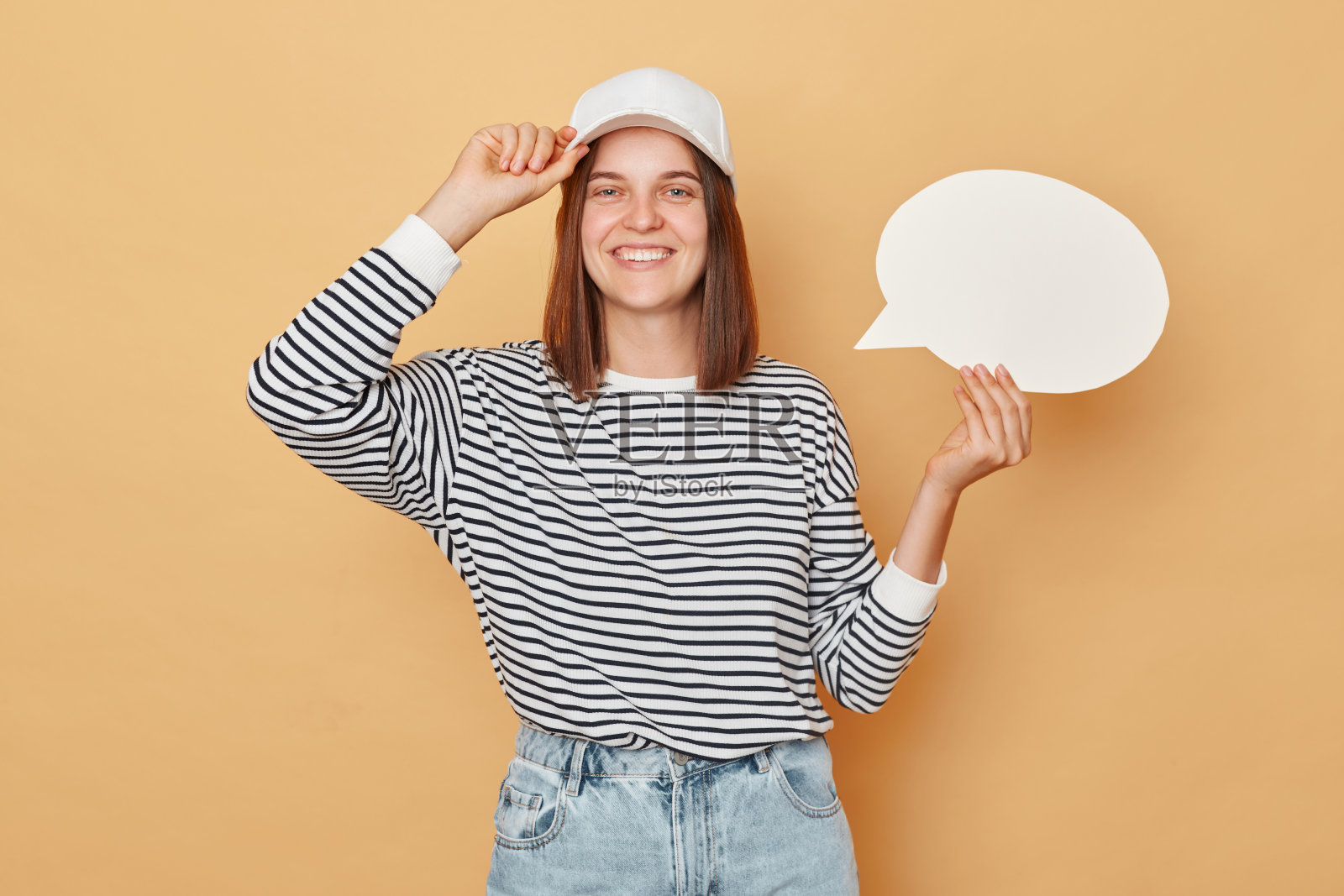 积极开朗微笑的女人戴着棒球帽和条纹衬衫拿着空泡泡演讲云孤立在米色背景复制空间为推广照片摄影图片