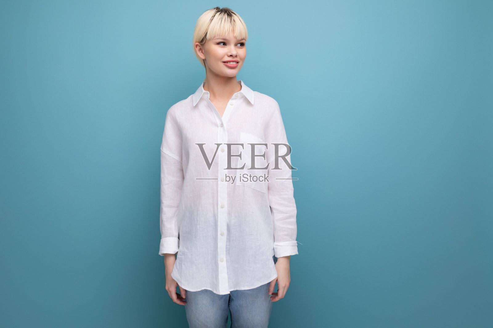 年轻成功的金发碧眼的职业女性,穿着白衬衫,自信地看着远处的蓝色背景和复制空间。人们的生活方式理念照片摄影图片