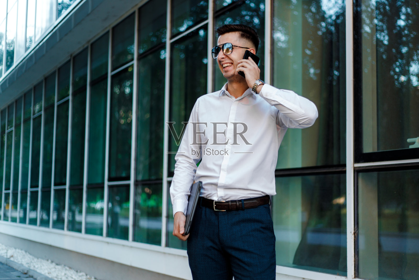 一位穿着白衬衫的年轻经理正在公司前面讲电话照片摄影图片