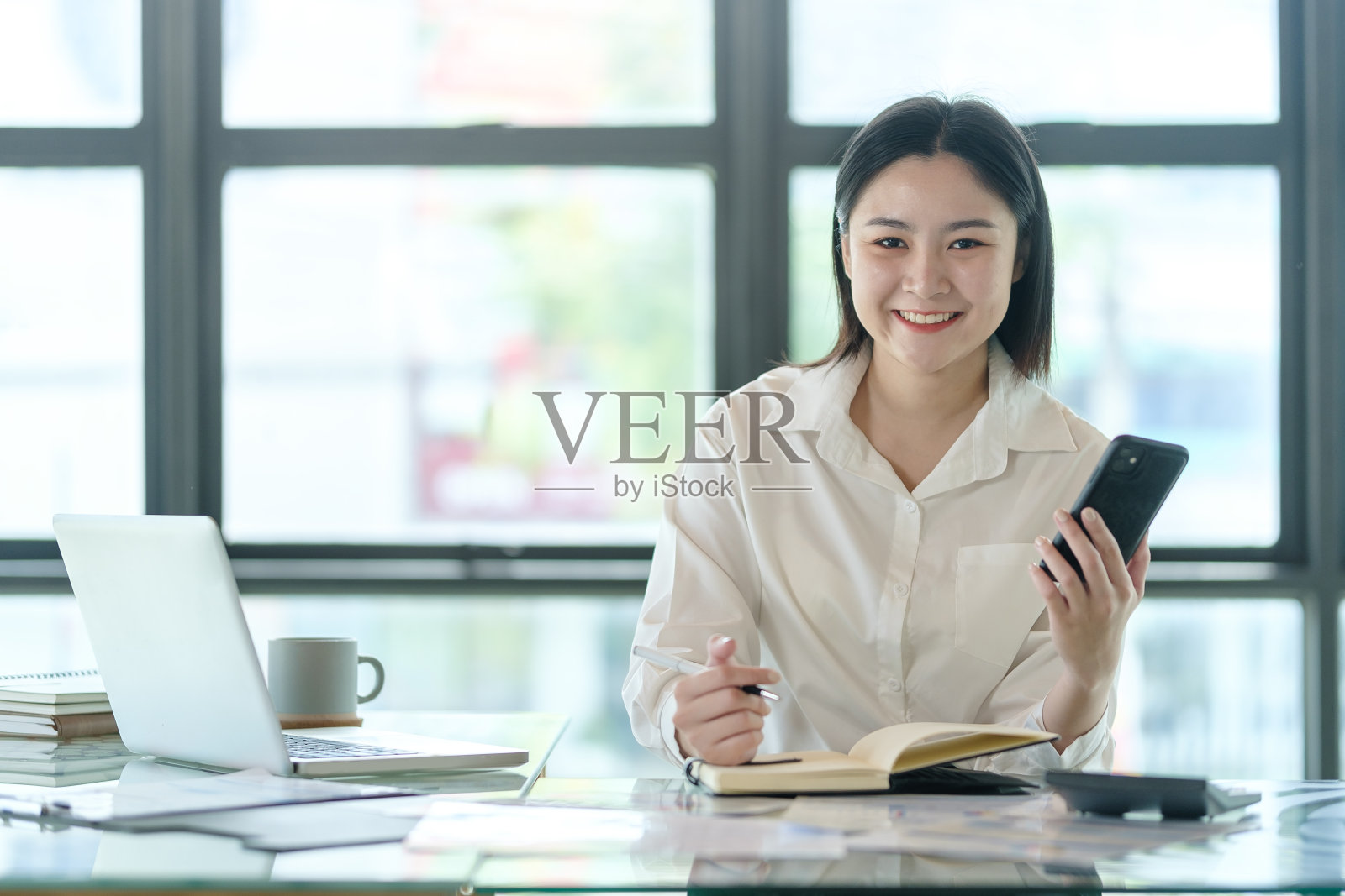 自信的千禧一代女性企业家坐在自己的私人办公室里,对着镜头微笑。照片摄影图片