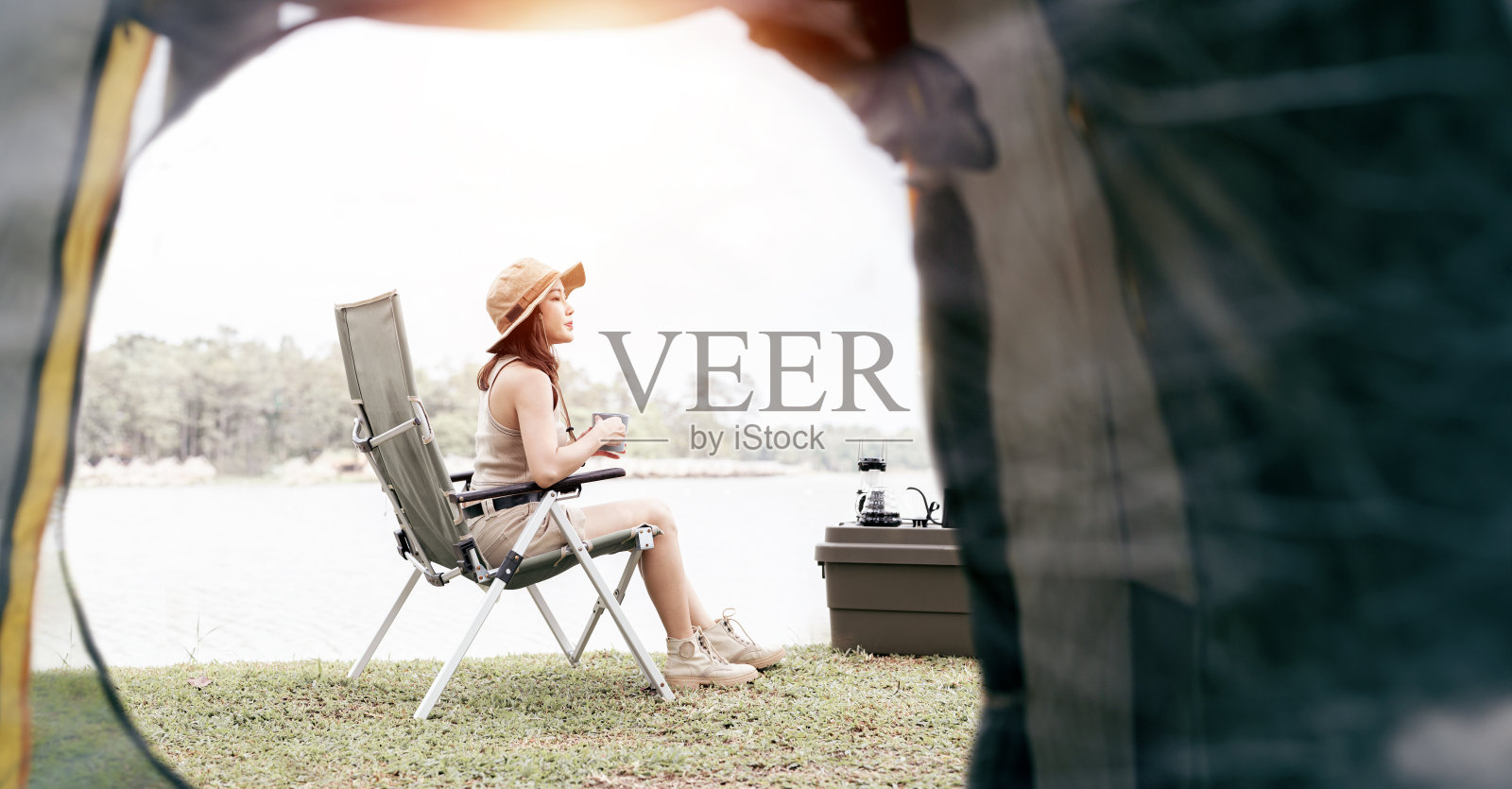 亚洲女人独自旅行和露营,坐在湖边的椅子上。照片摄影图片